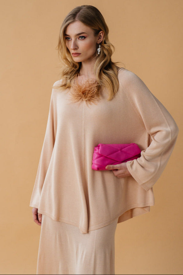 A model wearing a beige cape-style top with raglan long sleeves and a wide crew neckline, paired with skirt