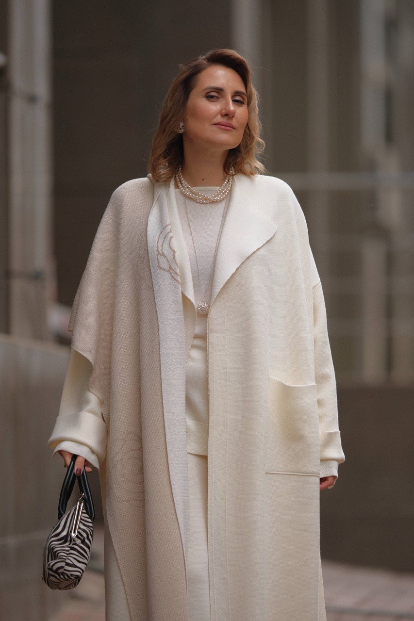Woman in a long beige coat holding a zebra-striped bag against a neutral background