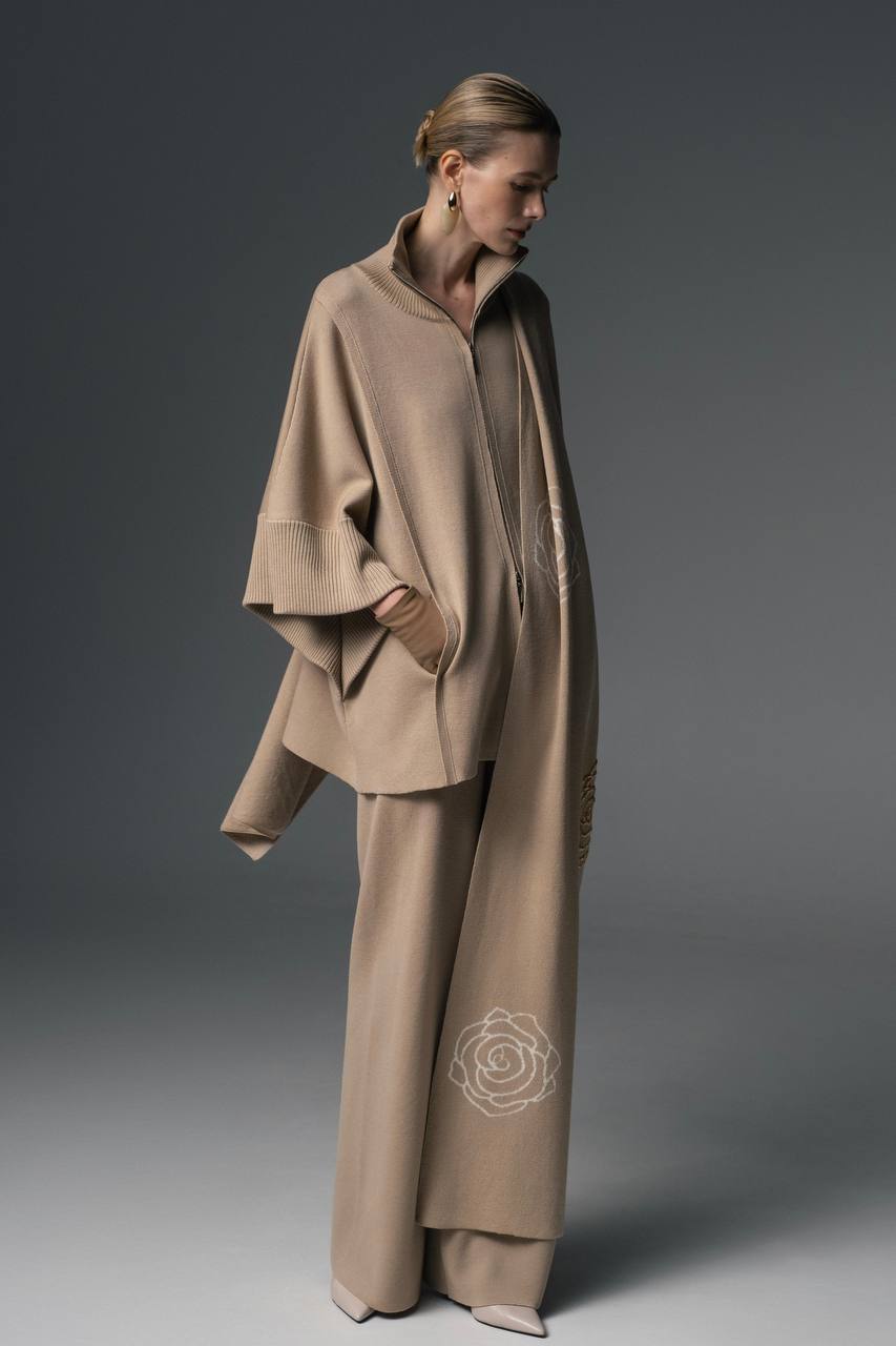 A person wearing a beige double zip-up coat with wide sleeves and a high collar, paired with matching pants.