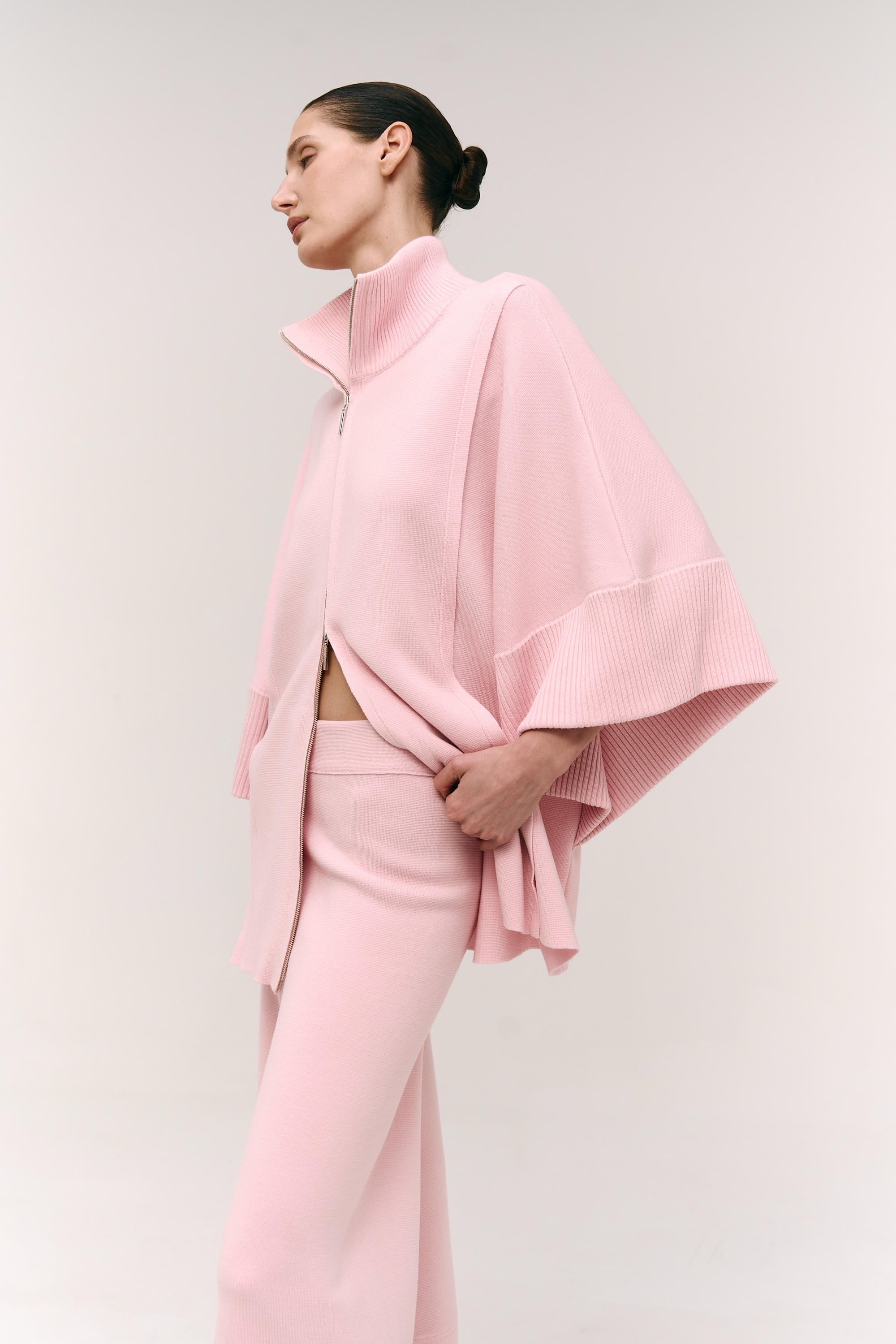 Person wearing a pink outfit with a cape against a plain background