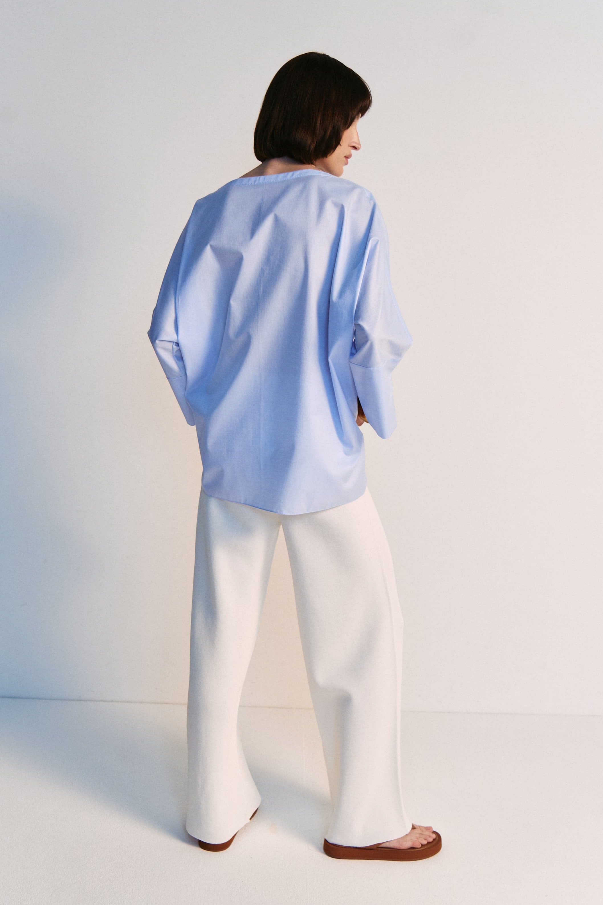 Person wearing a light blue shirt and white pants against a white background