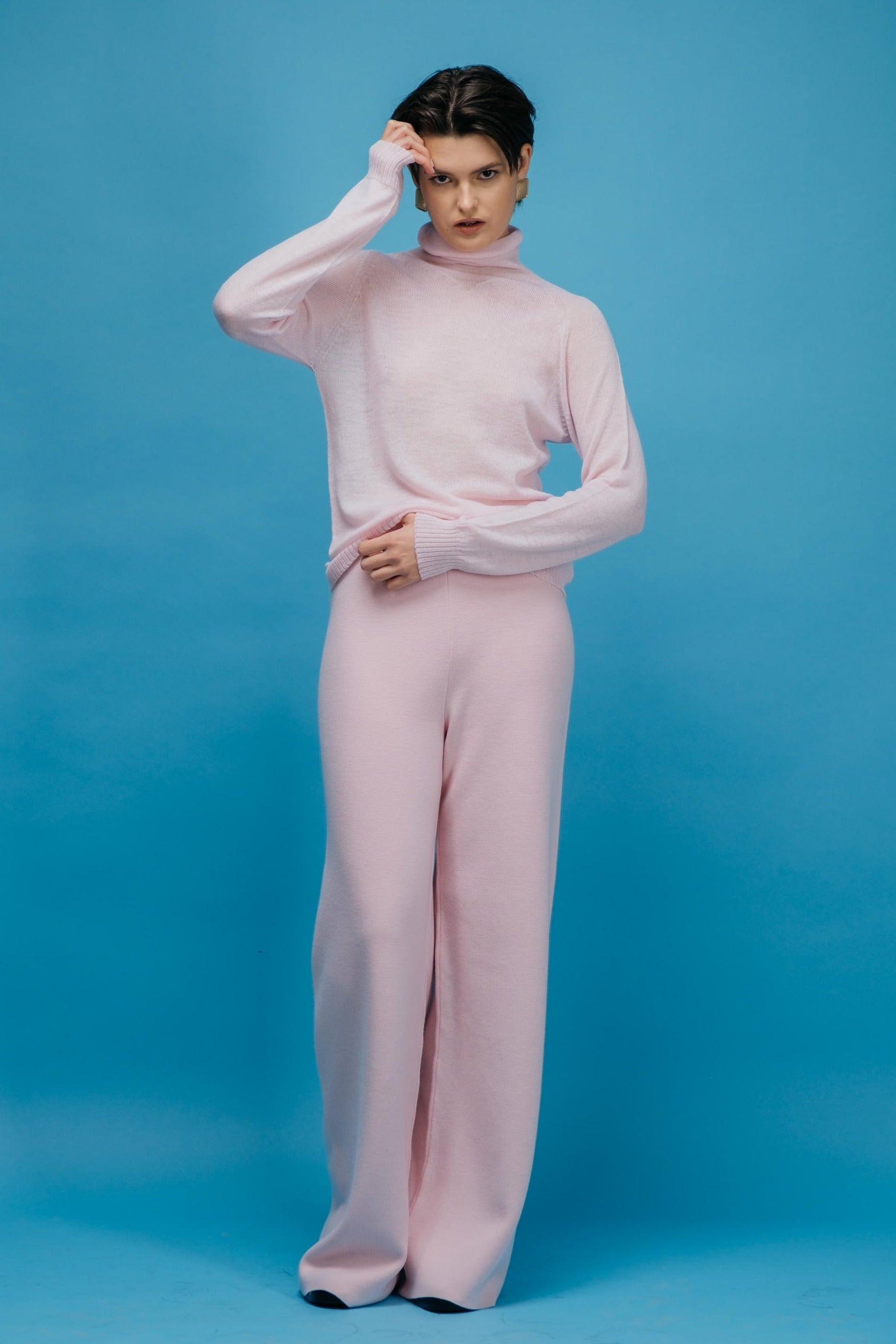 Person wearing a pink turtleneck and pants against a blue background