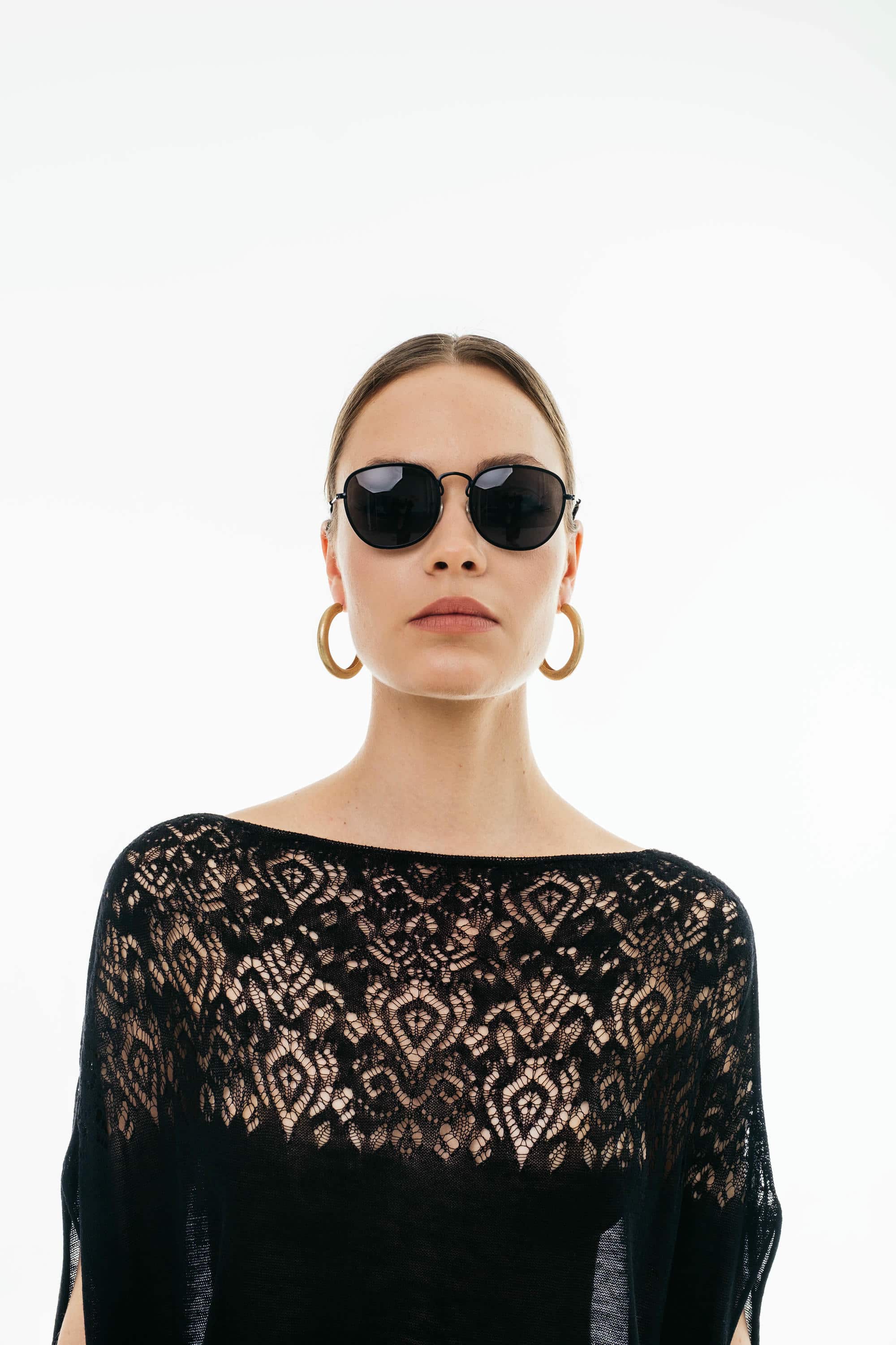 Woman wearing a black lace top and sunglasses on a white background