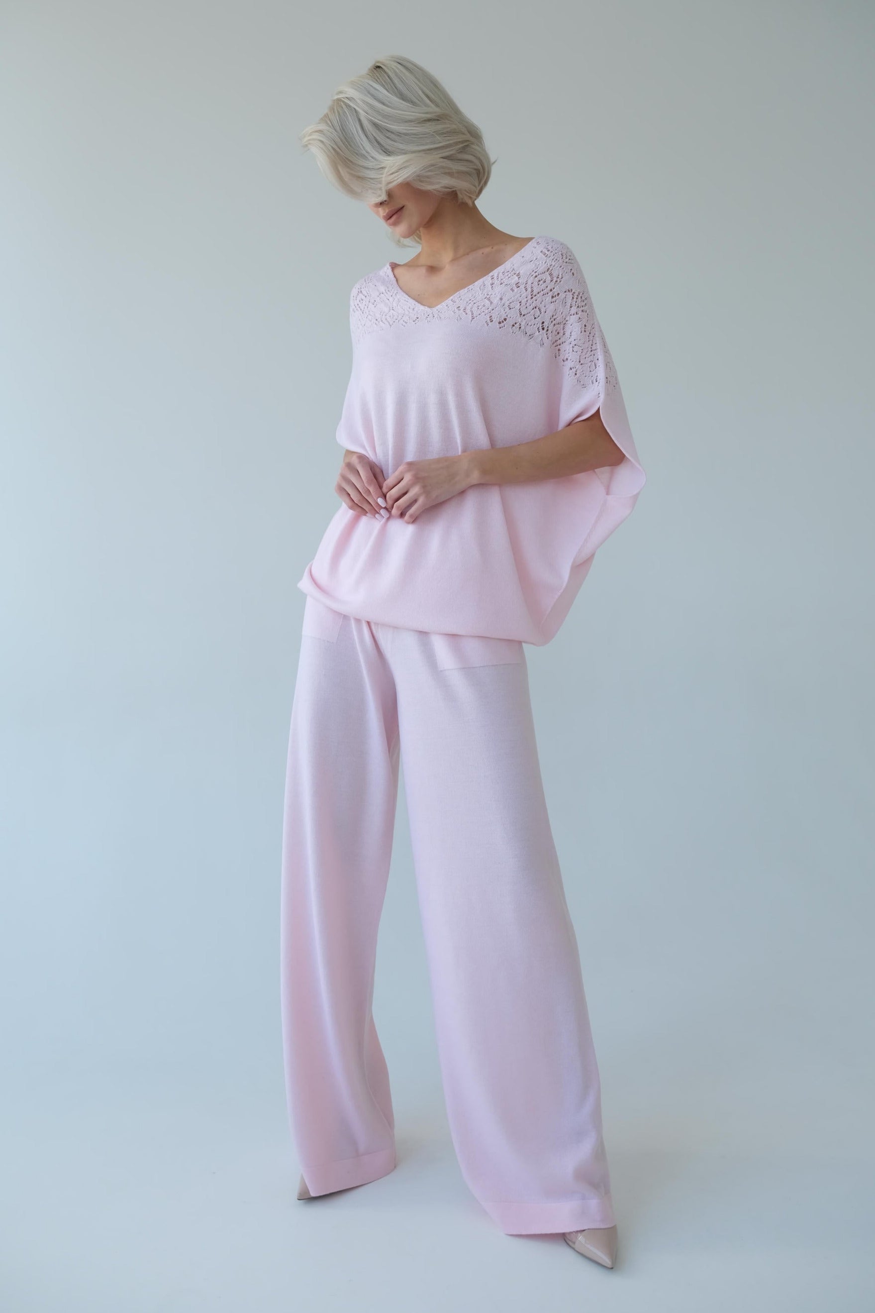 Woman wearing a light pink outfit with lace details on a white background