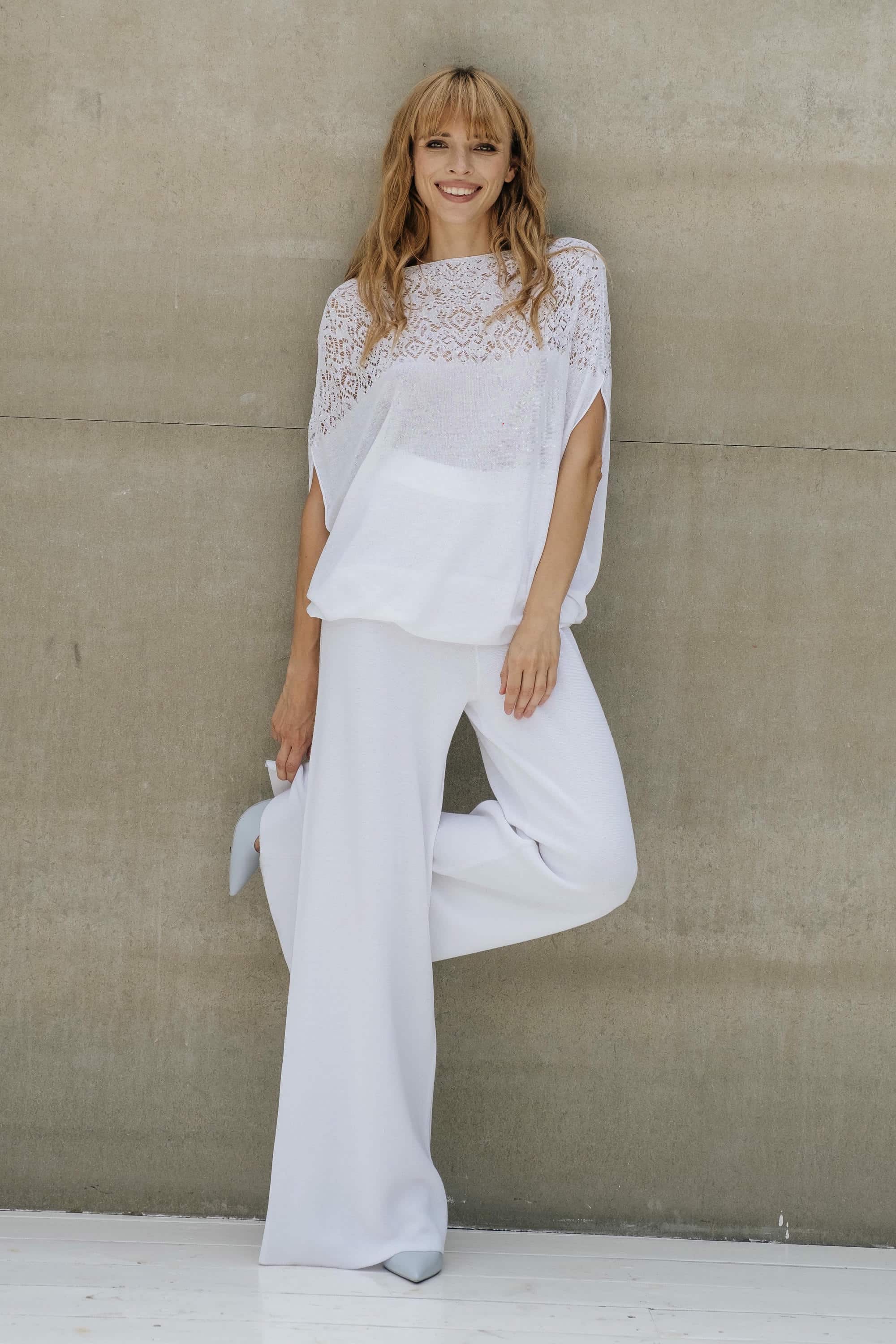 Woman in a white outfit standing against a beige wall
