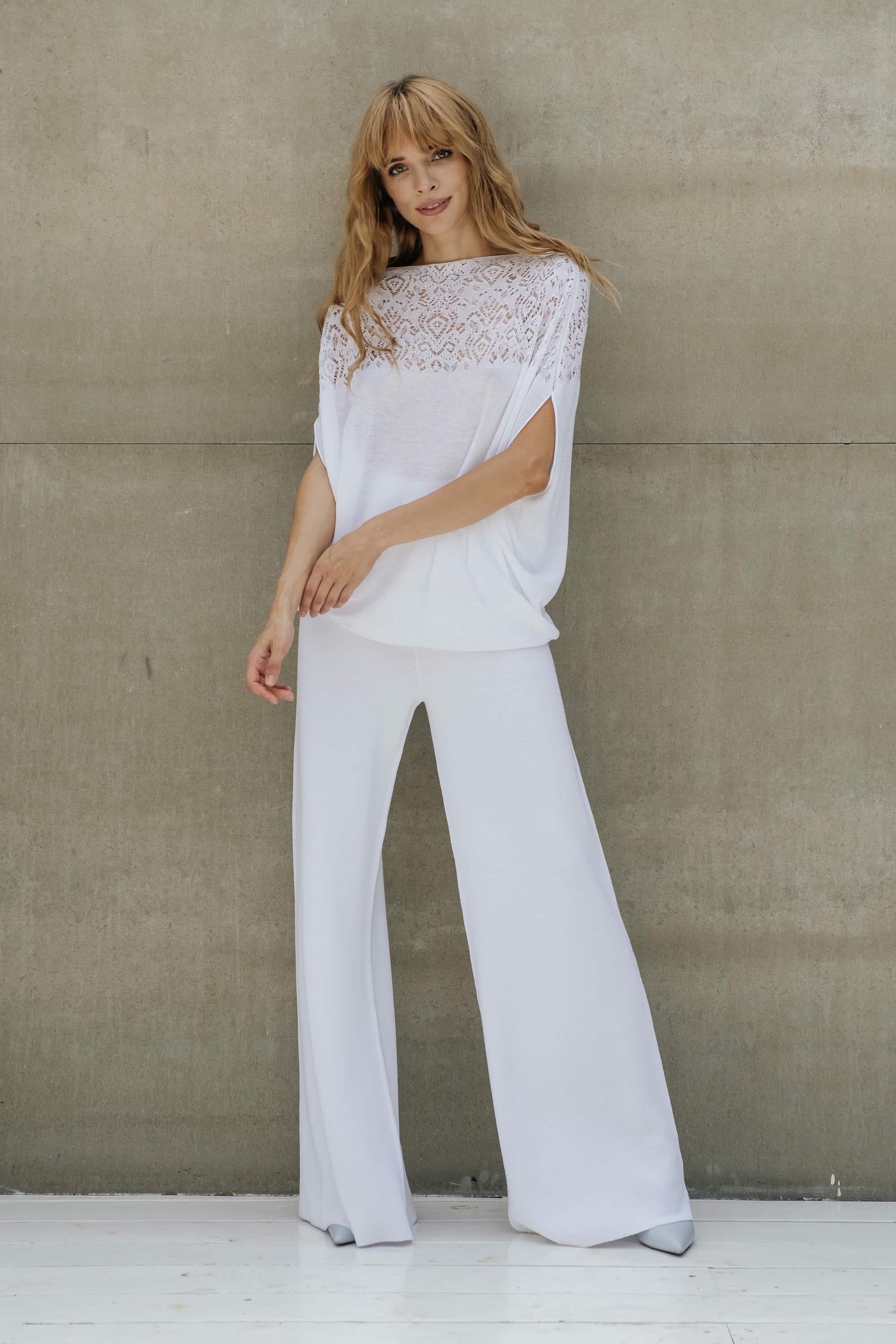 Woman wearing a white outfit with lace details against a plain background