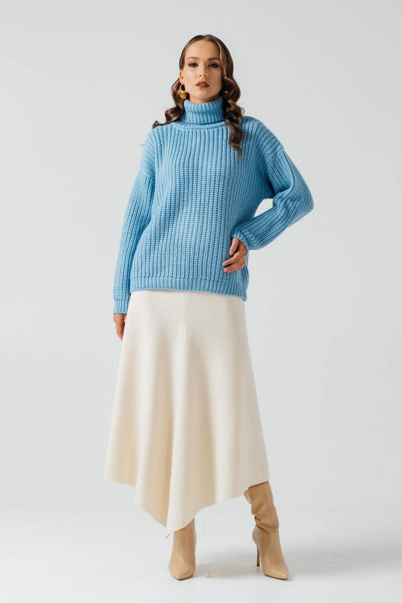 Woman wearing a blue sweater and beige skirt on a white background