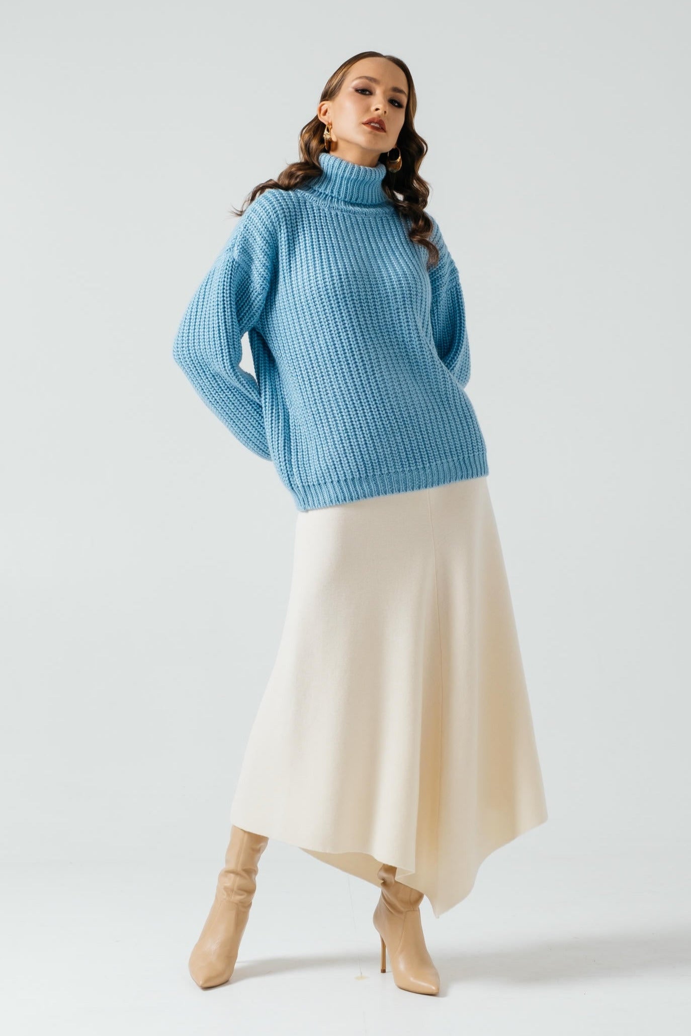Woman wearing a blue sweater and beige skirt on a white background