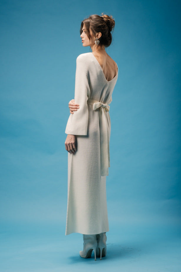 Woman wearing a long, light-colored dress with a bow on a blue background
