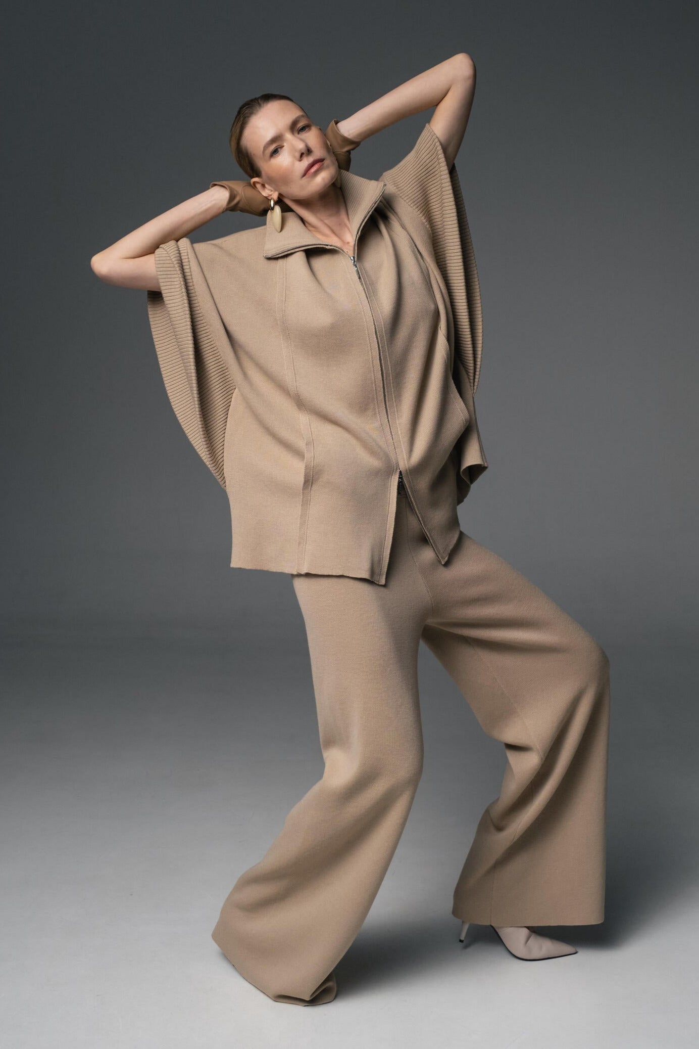 Woman wearing a beige outfit posing against a gray background