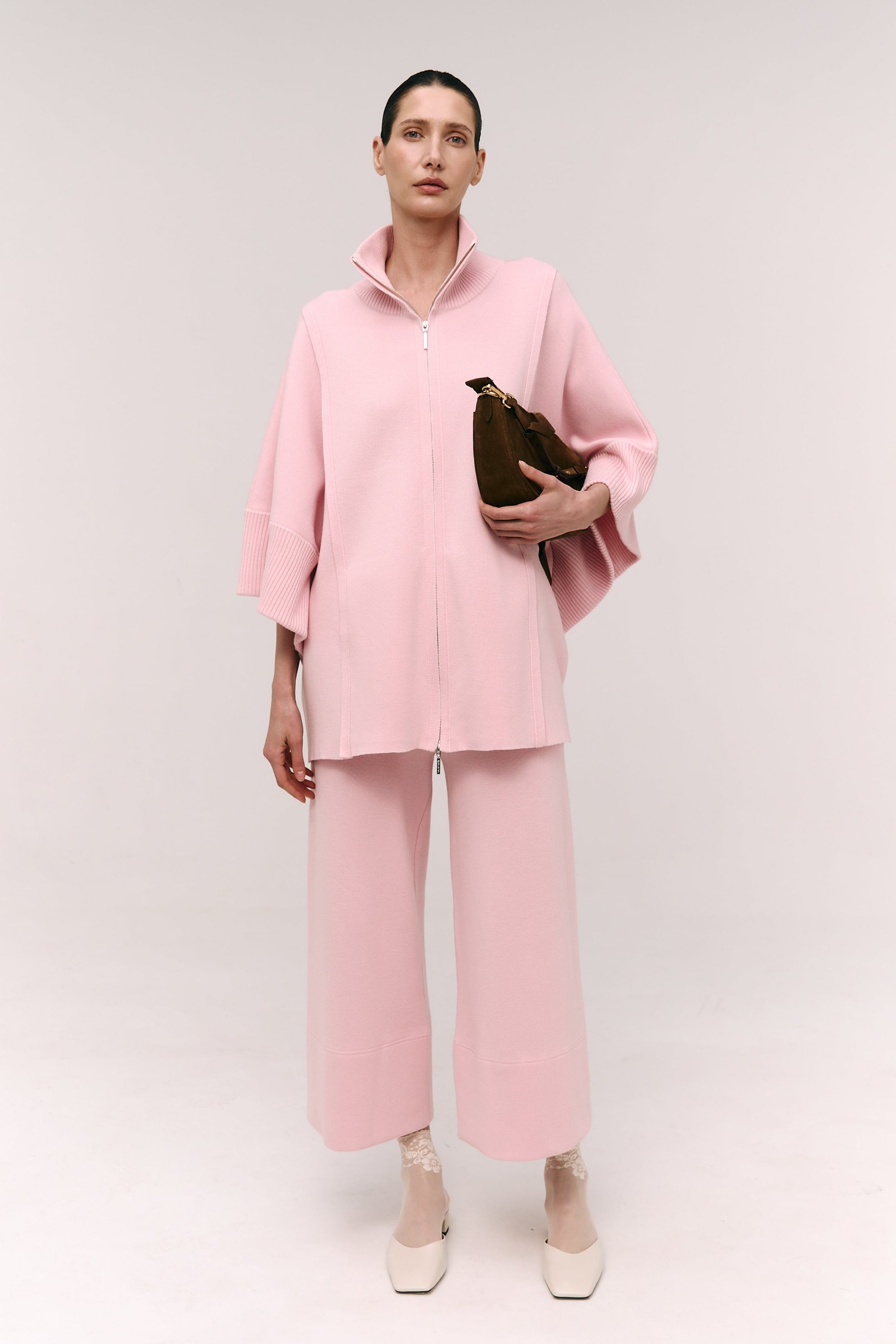 Person wearing a pink outfit holding a brown bag on a white background