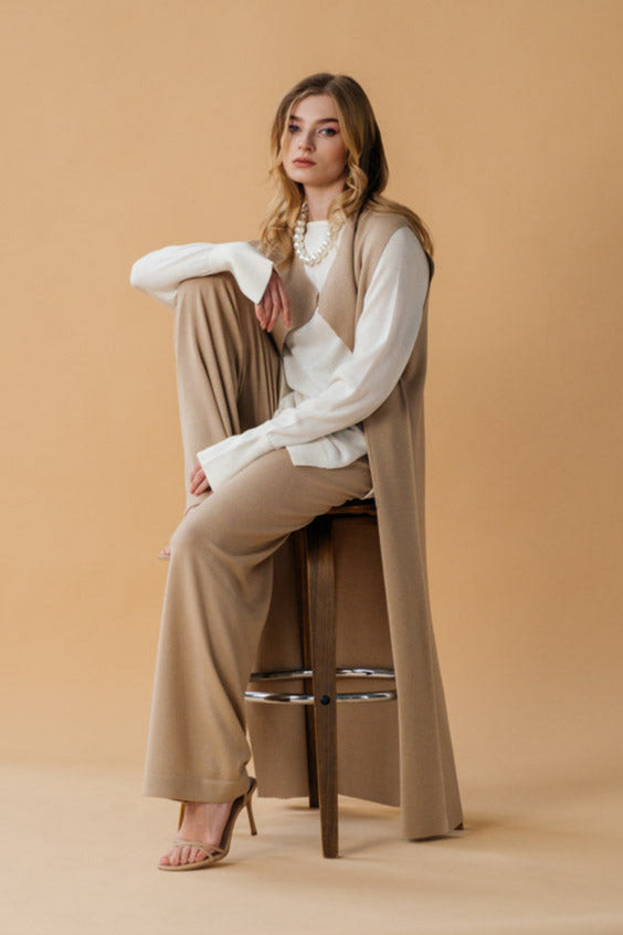 Woman sitting on a stool wearing a beige outfit against a beige background