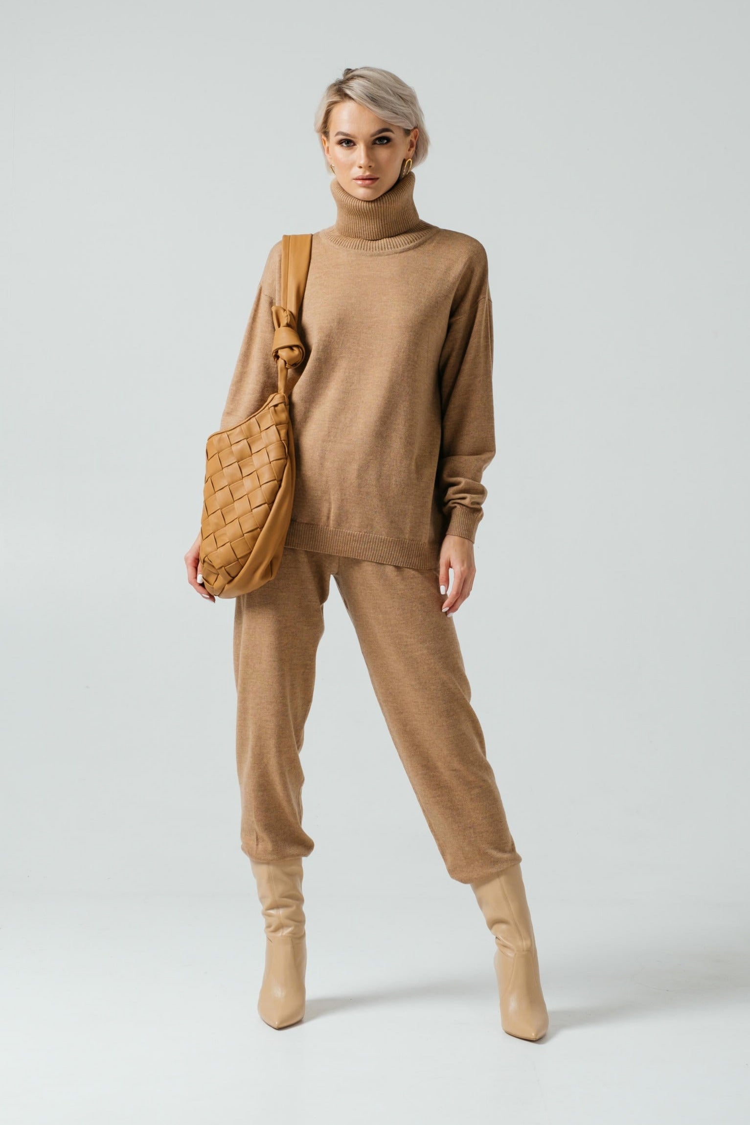 Woman wearing a beige sweater and pants with a matching handbag on a white background