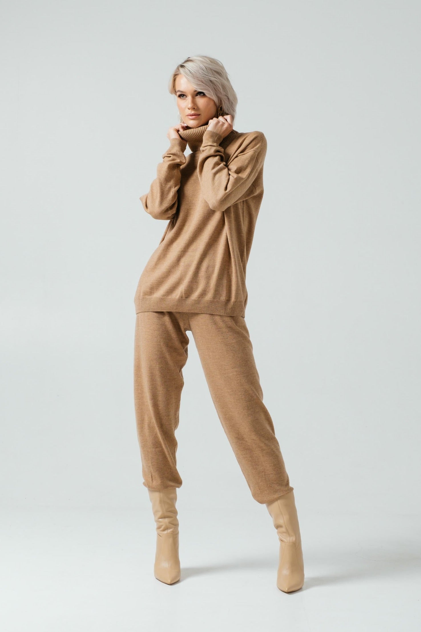 Woman wearing a beige outfit with a sweater and pants on a white background