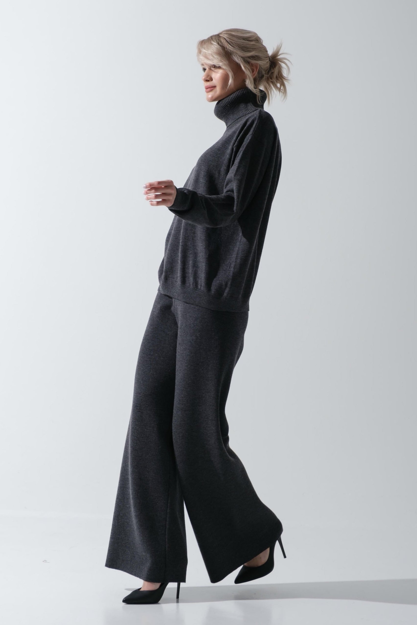 Woman wearing a dark gray turtleneck and wide-leg pants on a white background