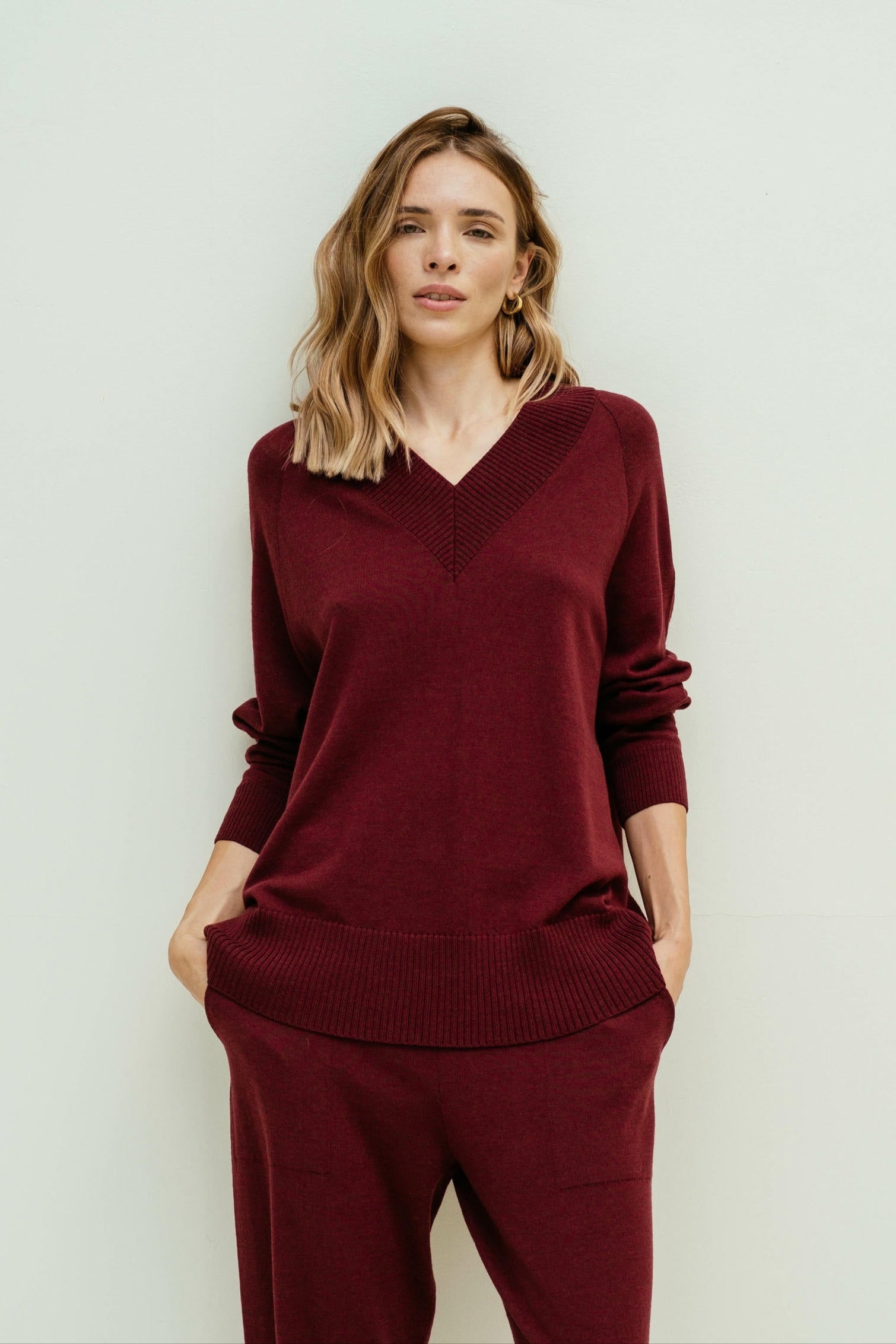 Woman wearing a burgundy sweater and pants against a white background