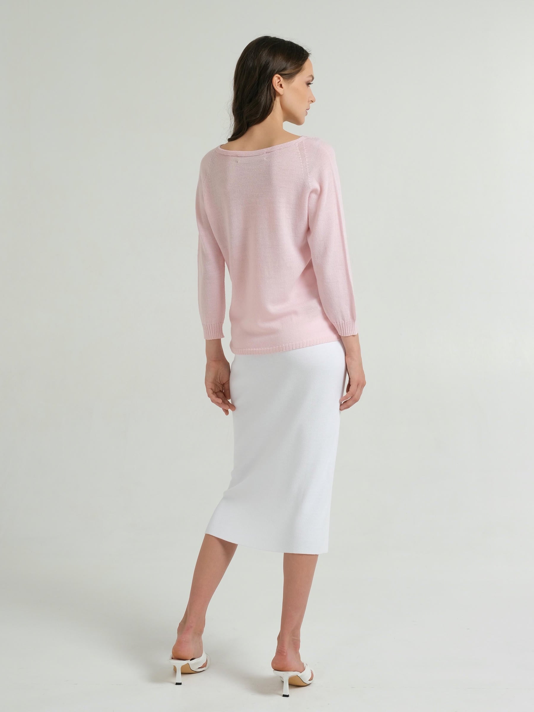 Woman wearing a light pink sweater and white skirt on a plain background