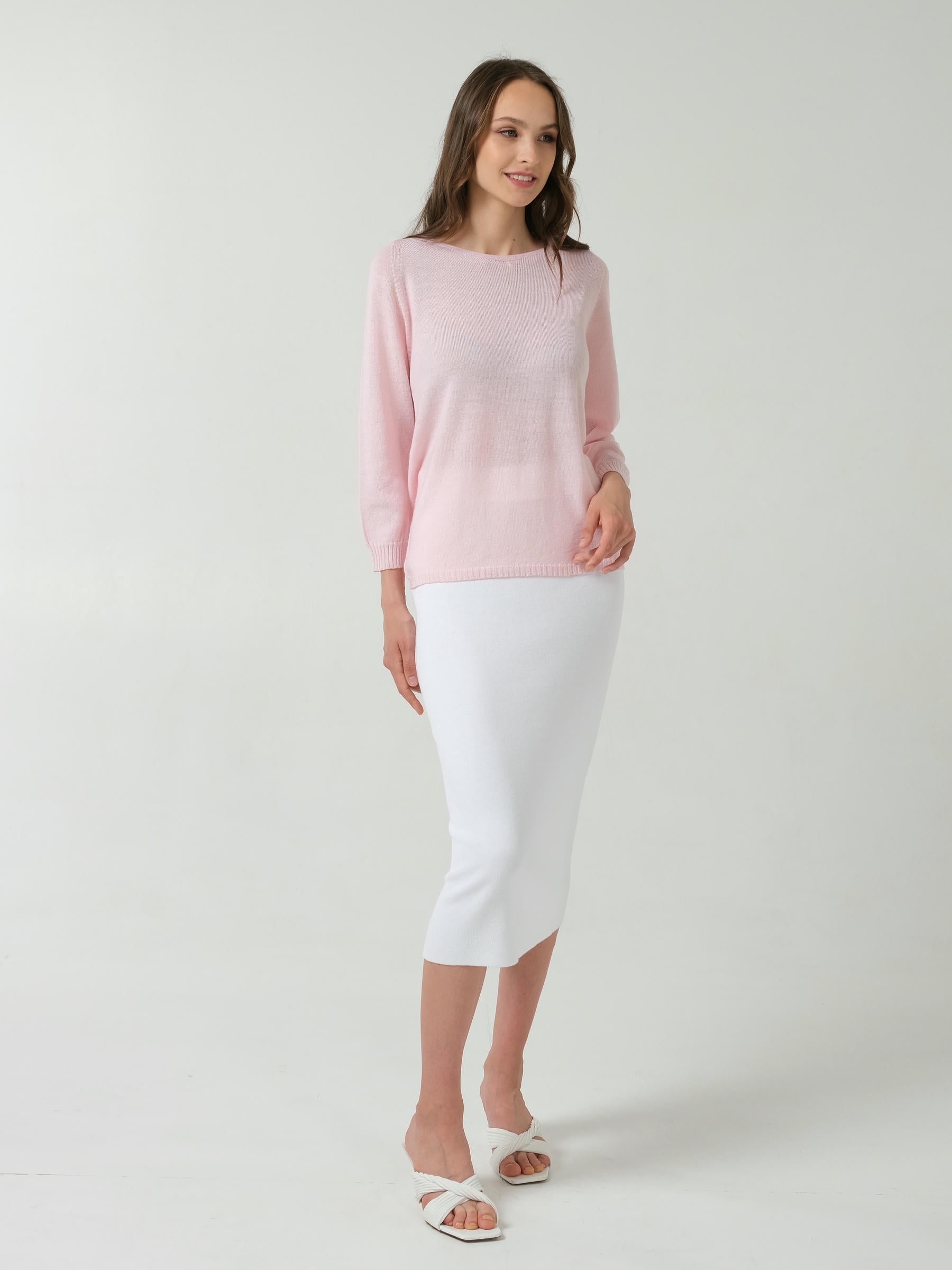 Woman wearing a light pink sweater and white skirt on a plain background