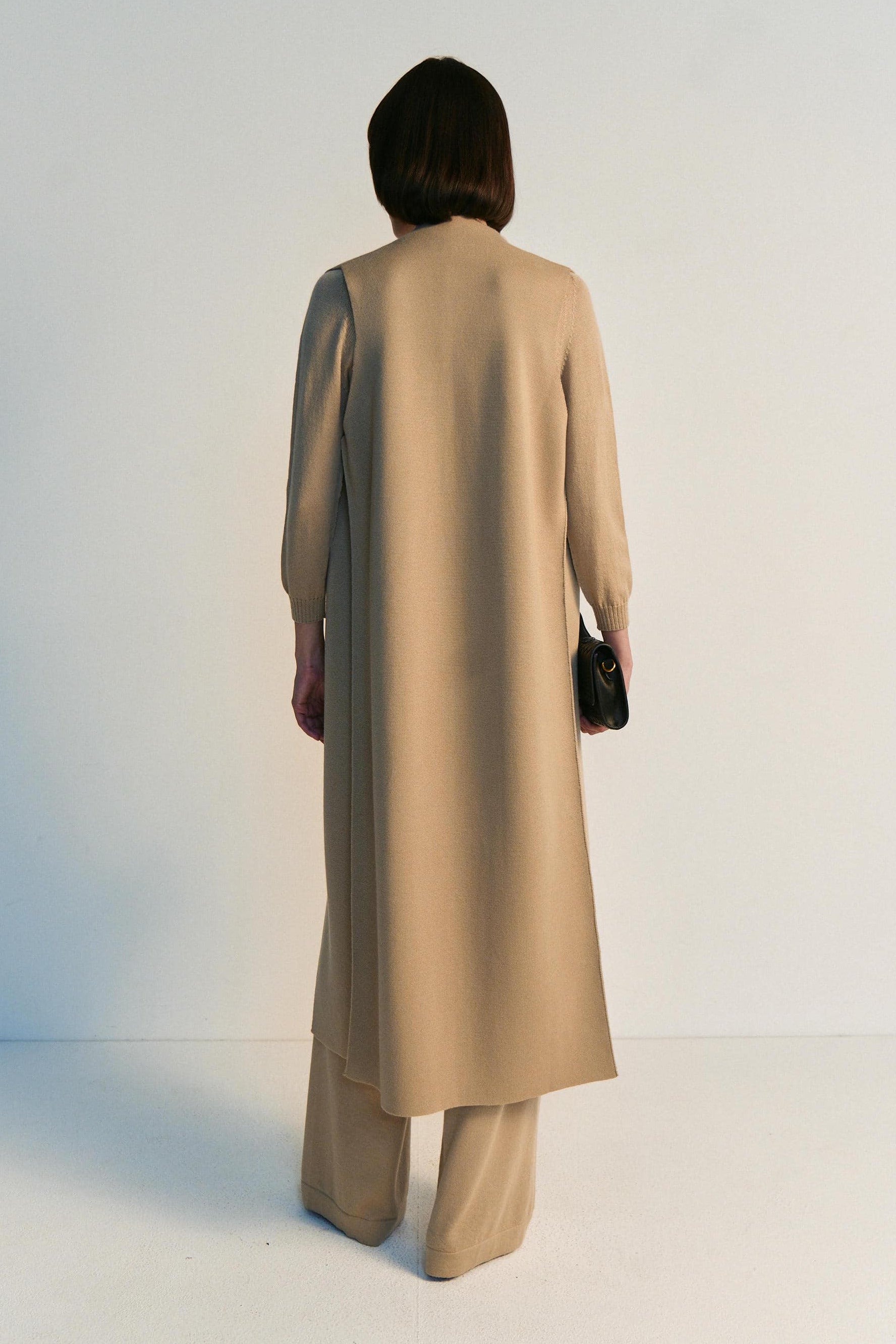 Person wearing a long beige coat on a white background