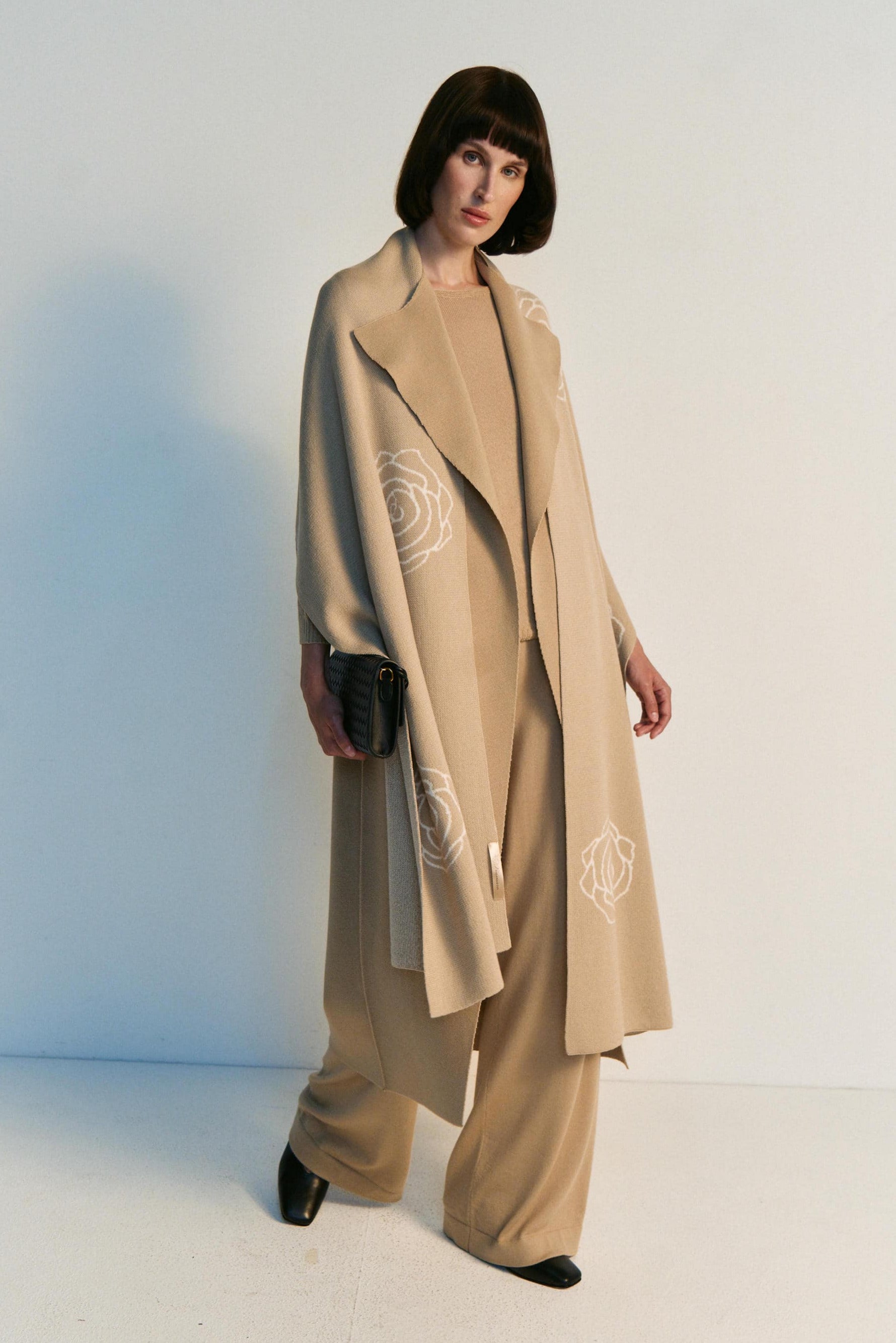 Woman wearing a beige coat with a brand logo, standing against a white background