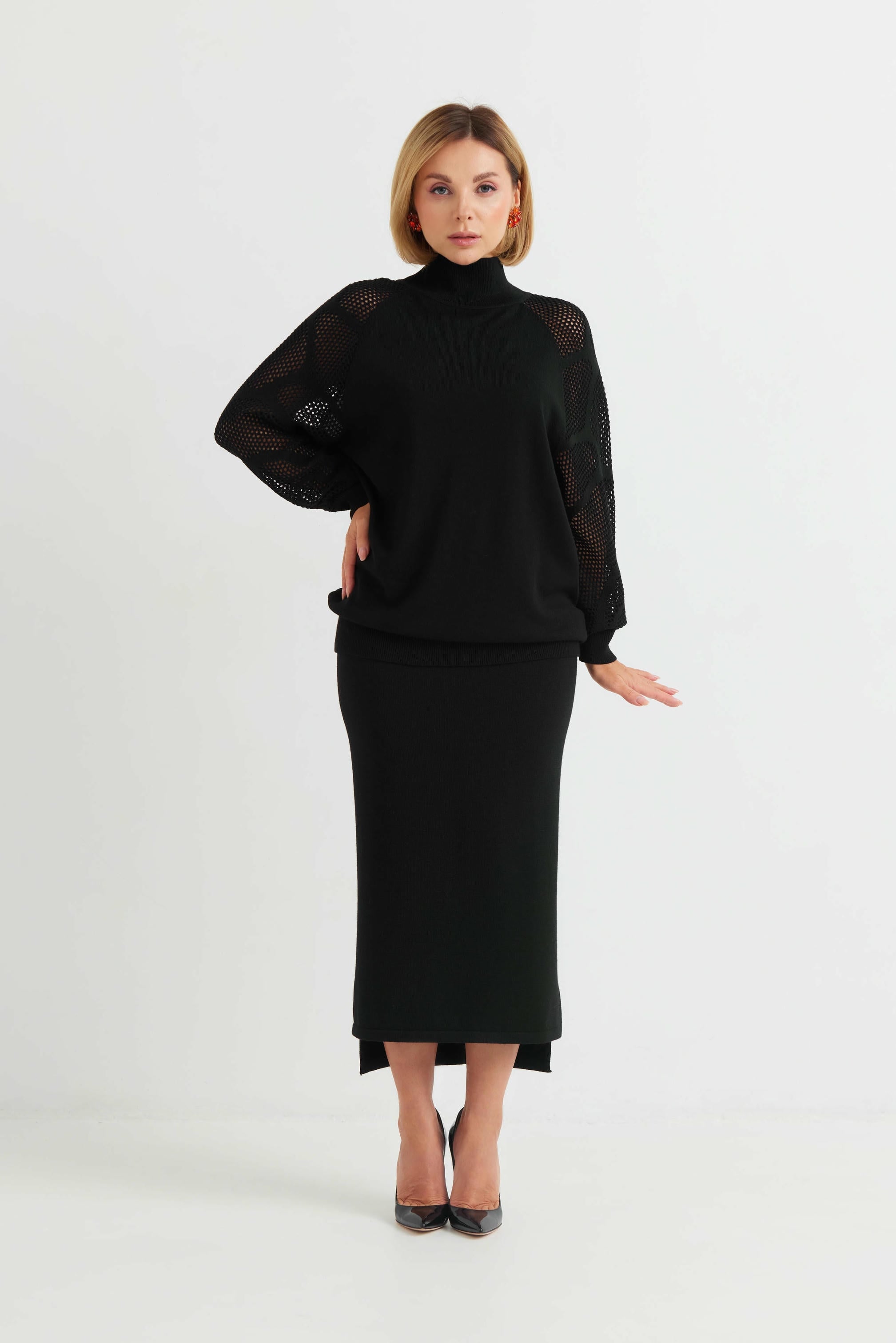 Woman wearing a black outfit with sheer sleeves on a white background
