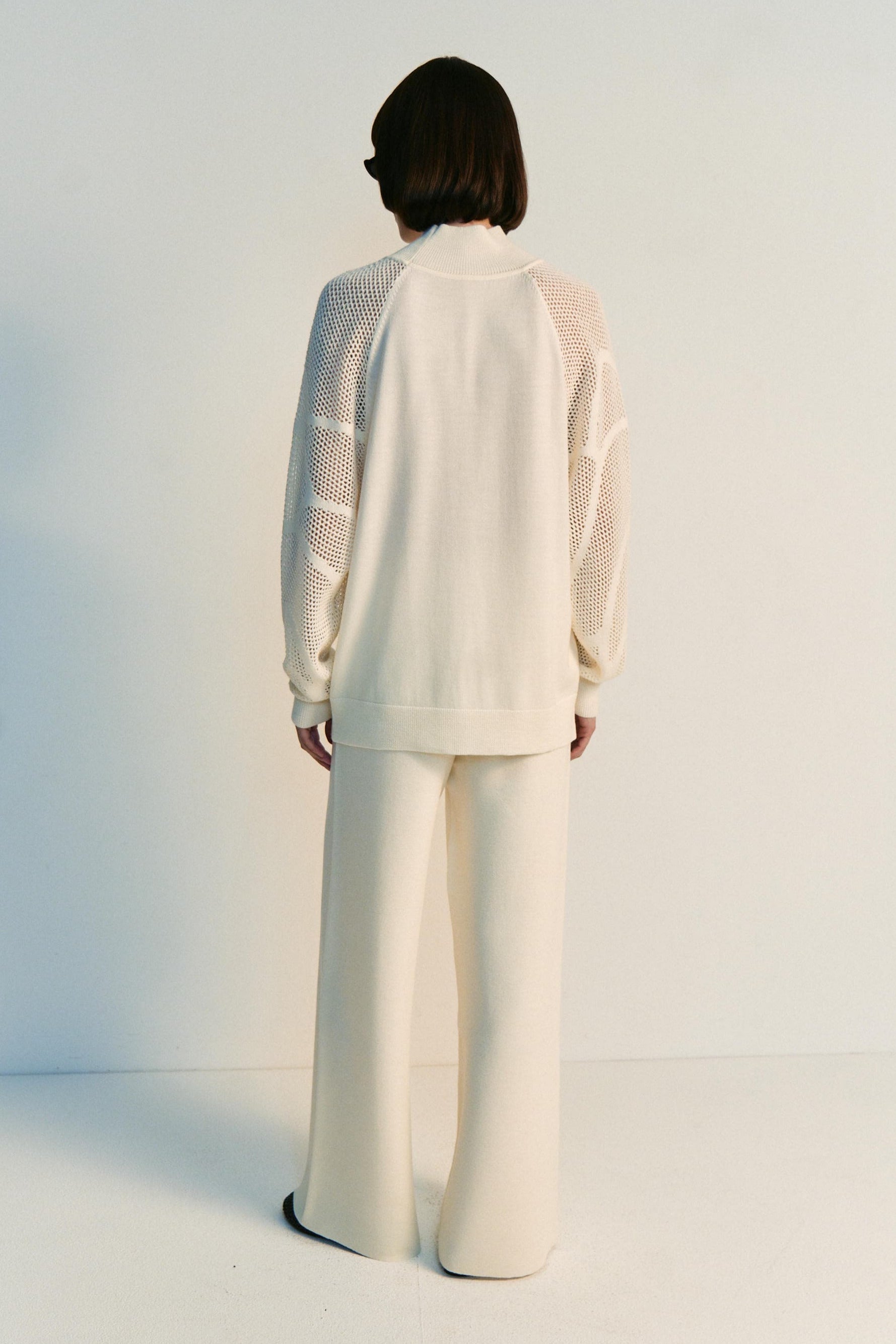 Person wearing a white outfit with sheer sleeves against a plain background