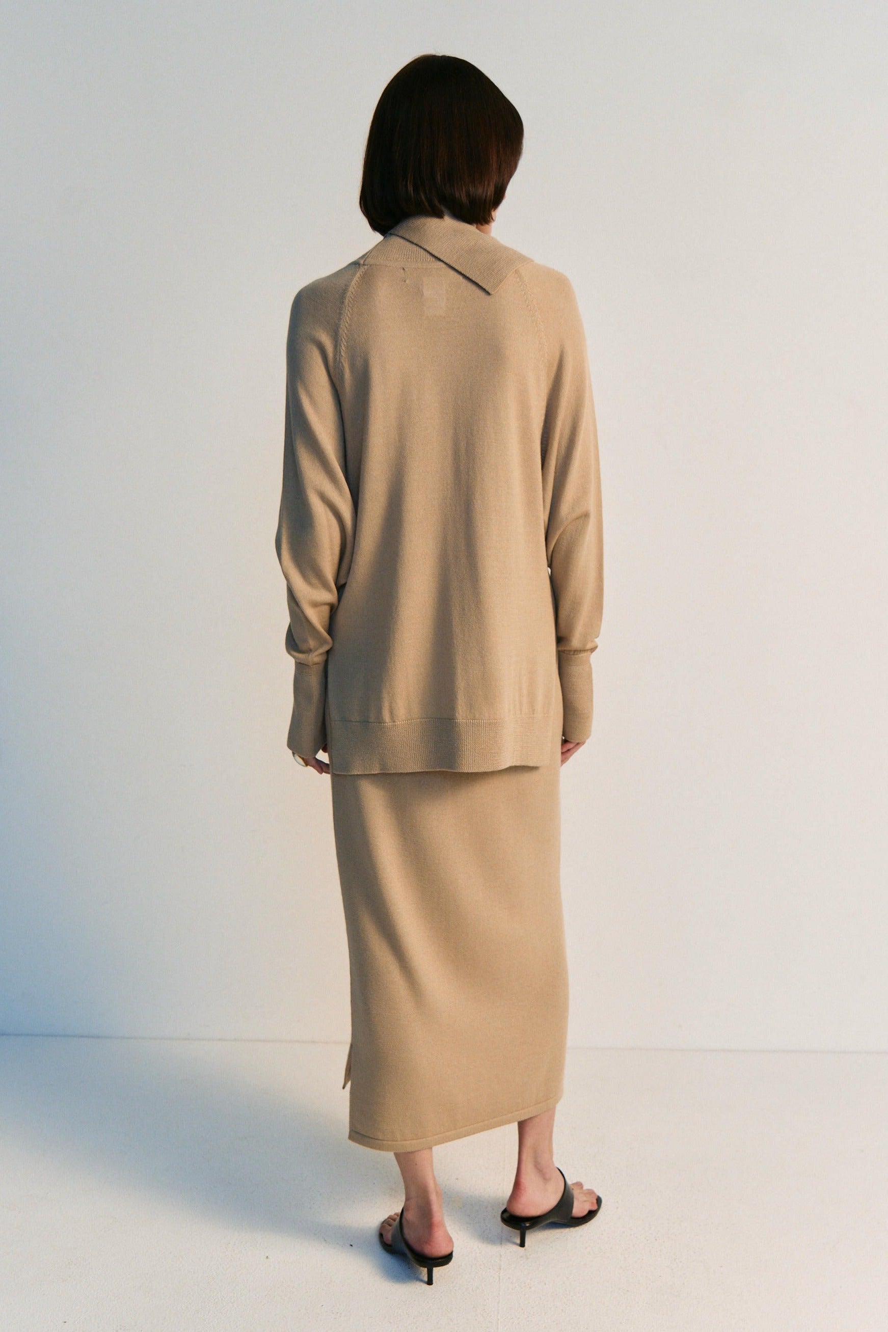Person wearing a beige suit standing against a white background