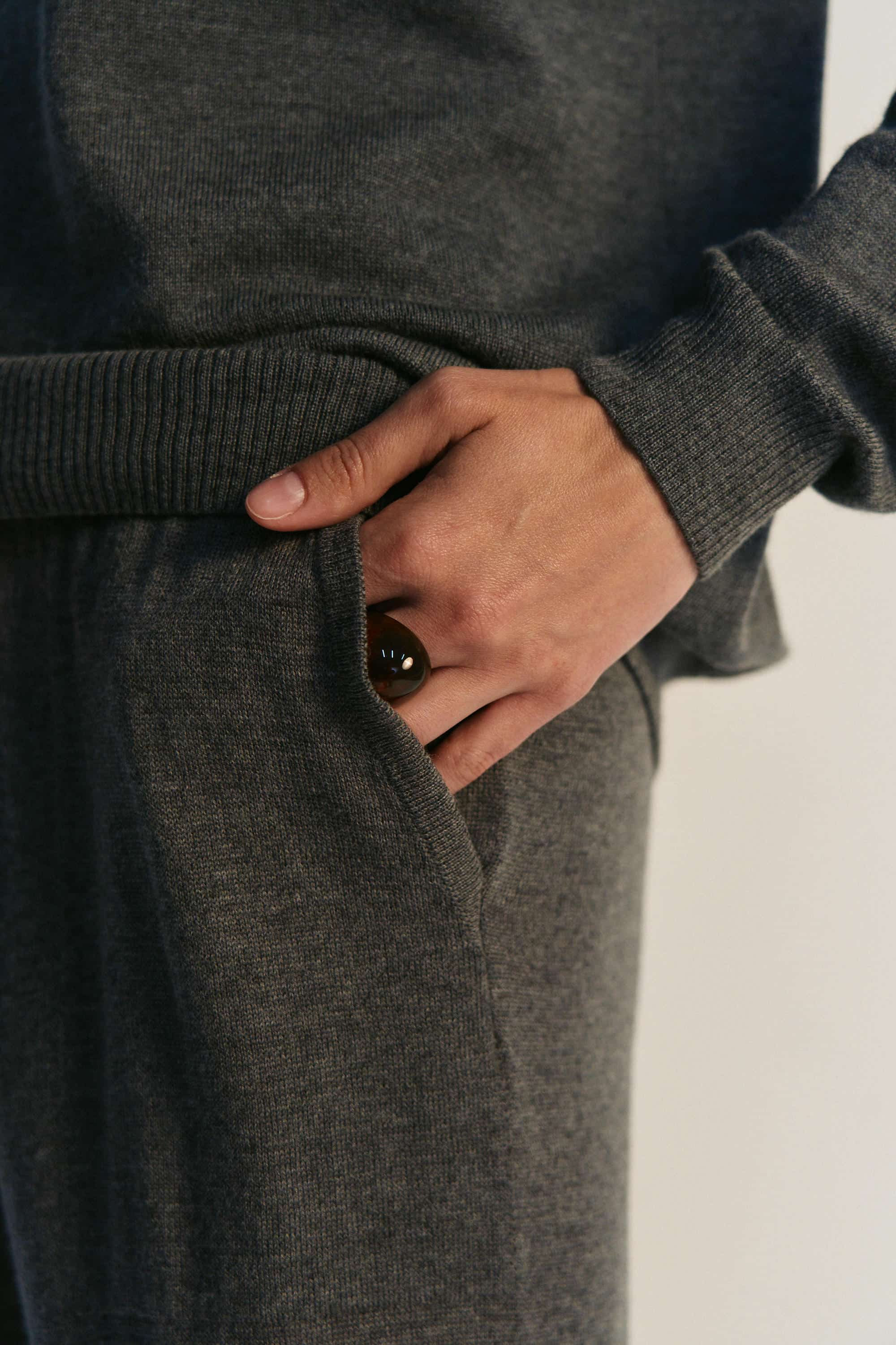 Person wearing a dark gray outfit with a close-up of a hand in a pocket.