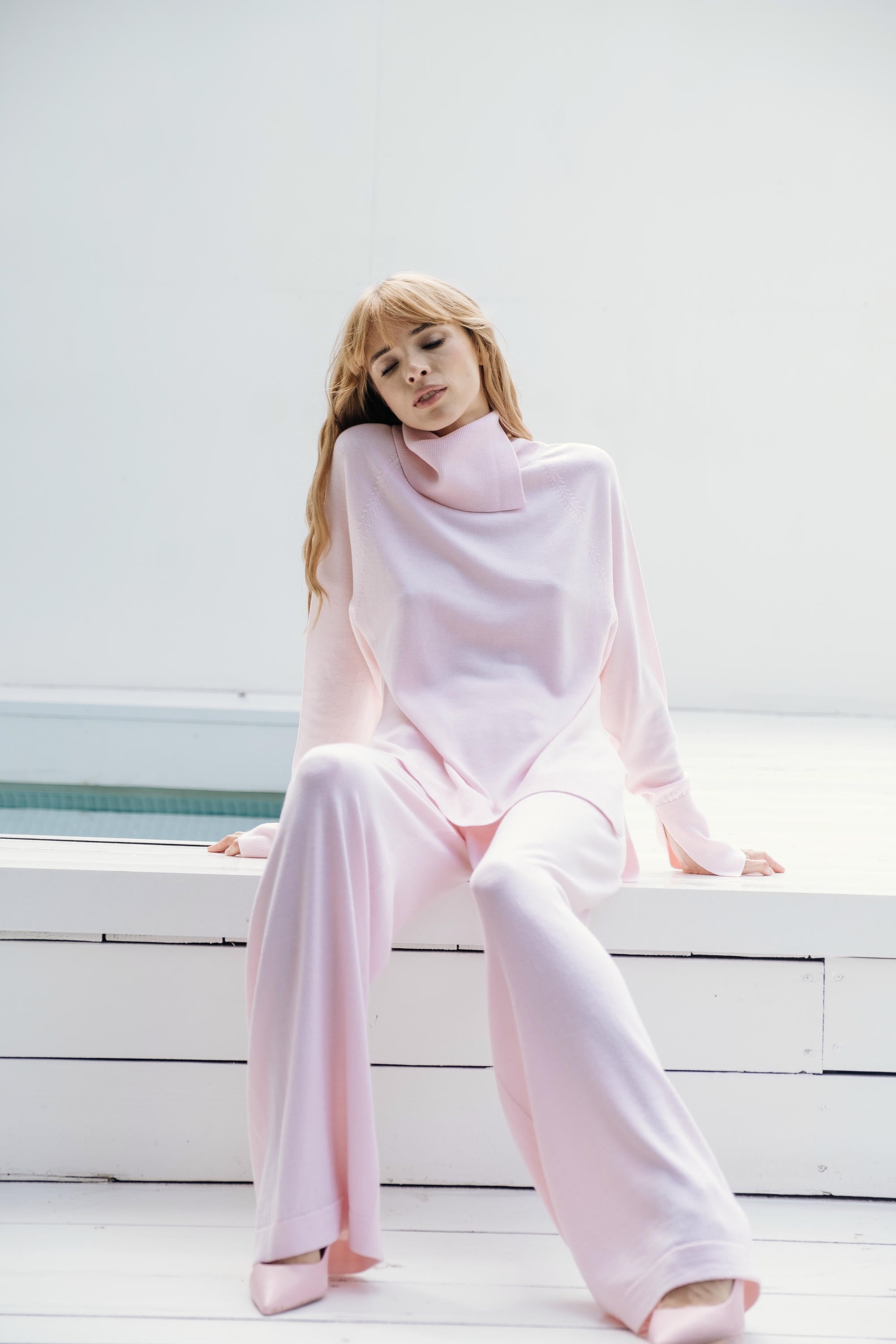 Woman wearing a light pink outfit sitting on white steps.