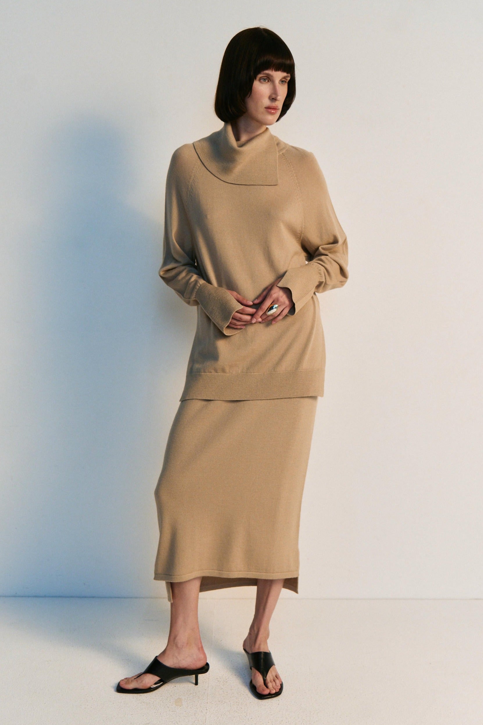 Person wearing a beige turtleneck and skirt set against a white background