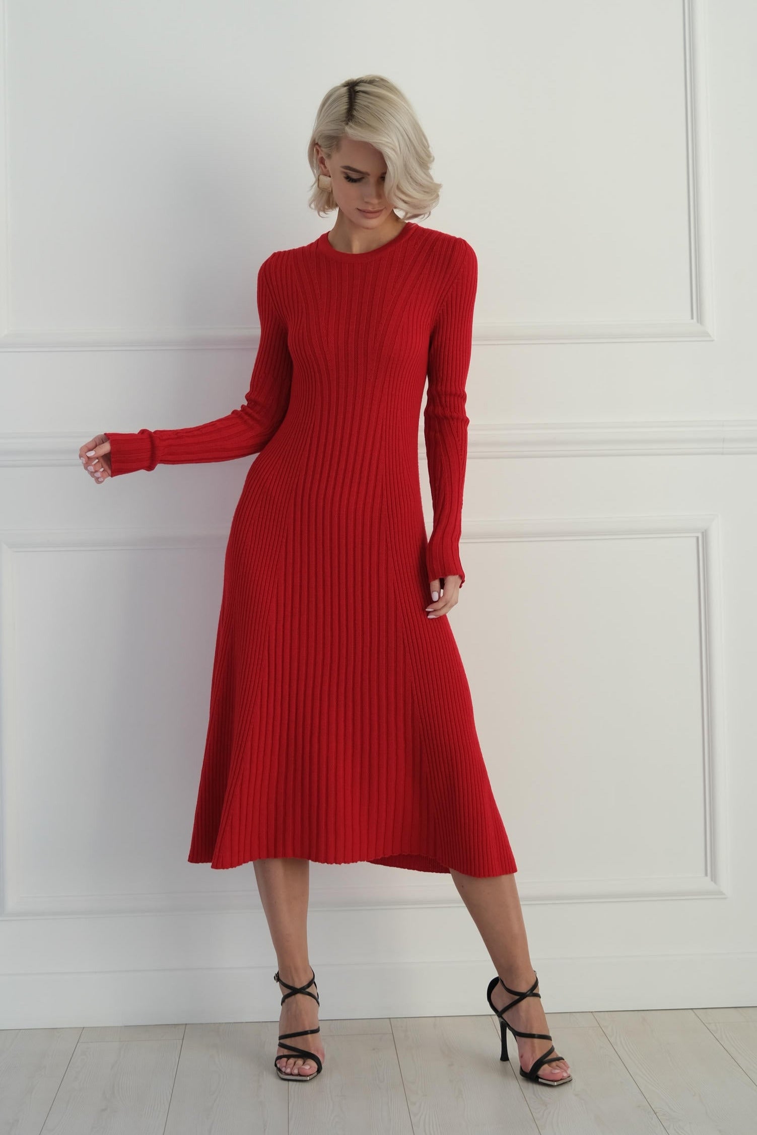 Woman wearing a red ribbed dress against a white paneled wall.