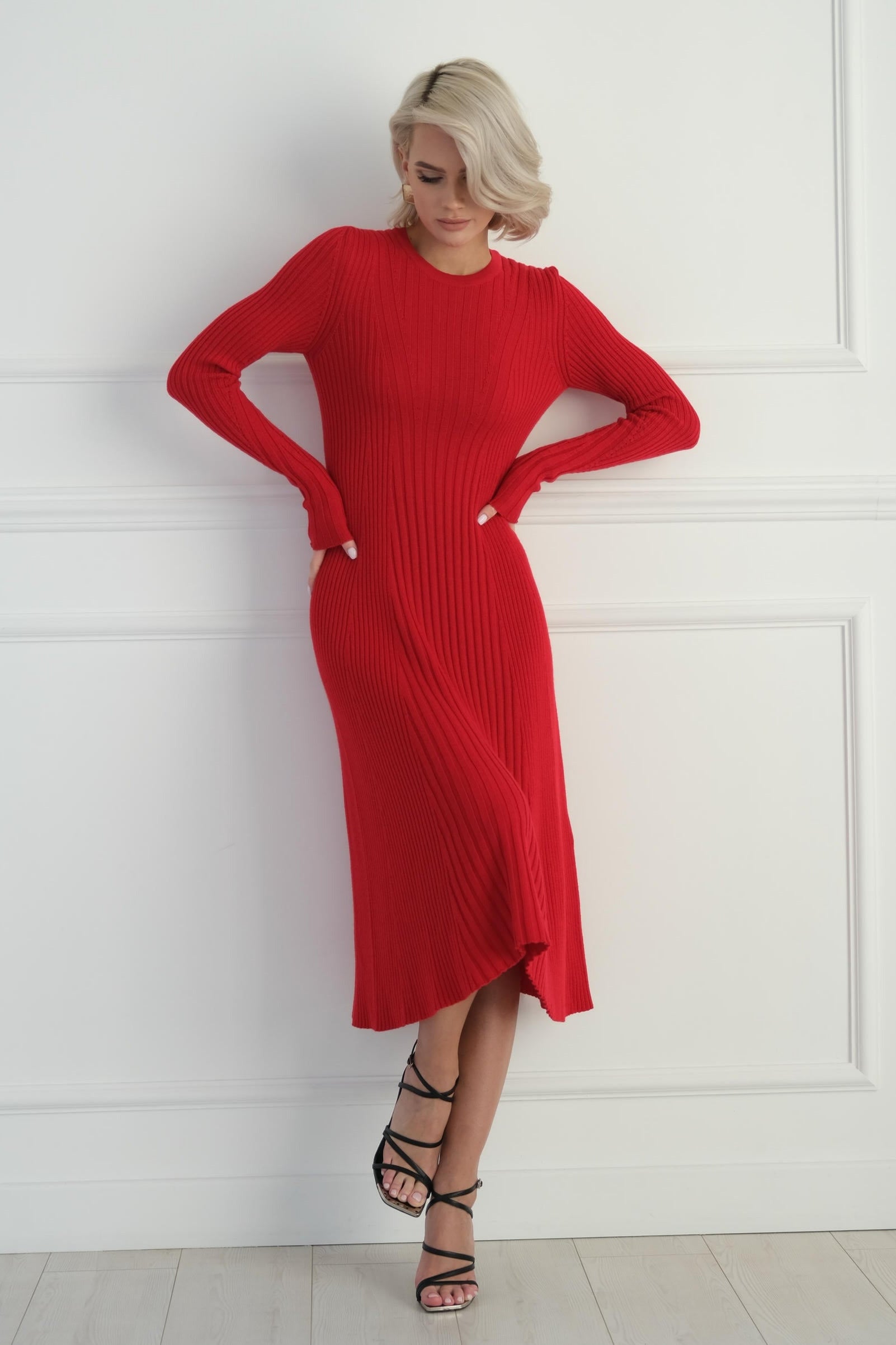Woman in a red dress standing against a white paneled wall.