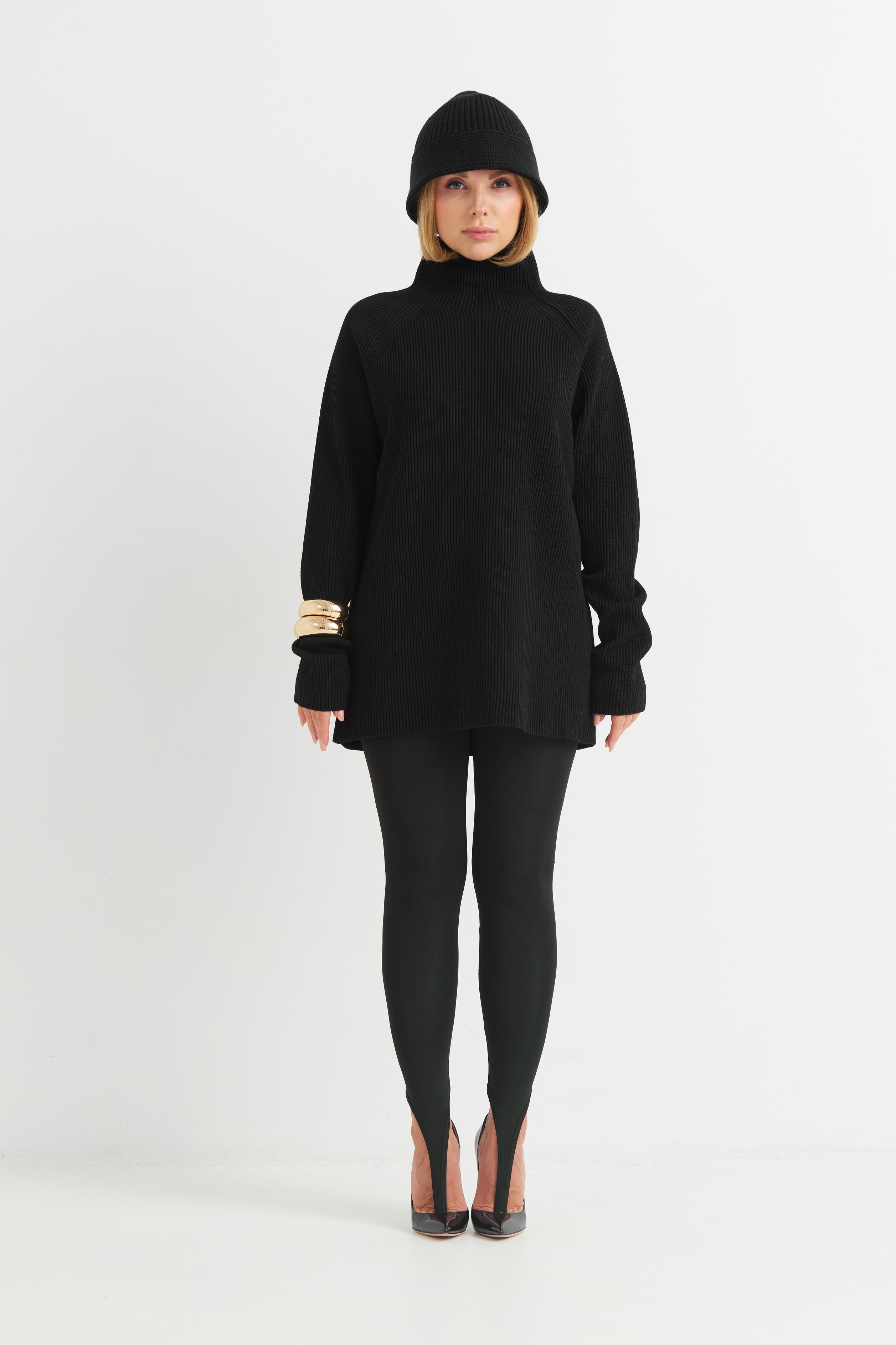 Person wearing a black outfit with a turtleneck sweater and leggings on a white background