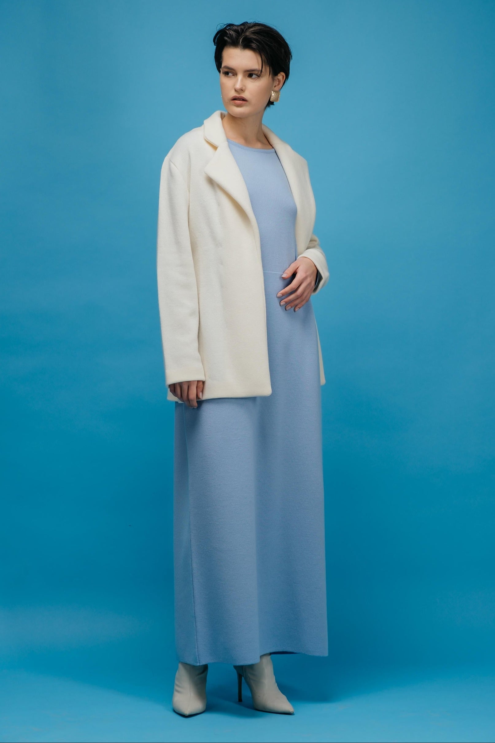 Woman wearing a light blue dress and cream coat against a blue background