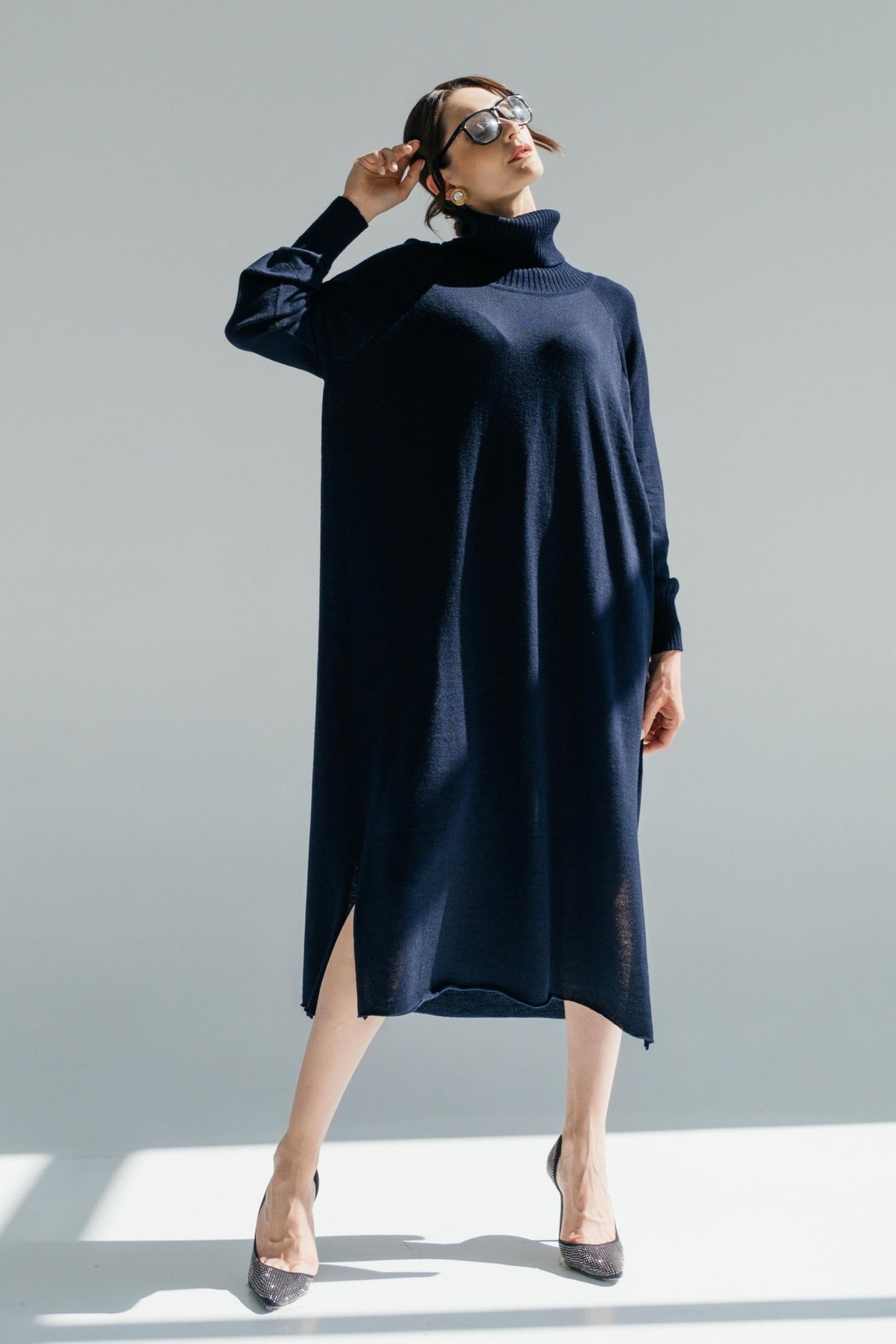 Woman wearing a navy blue dress with a high collar against a light gray background