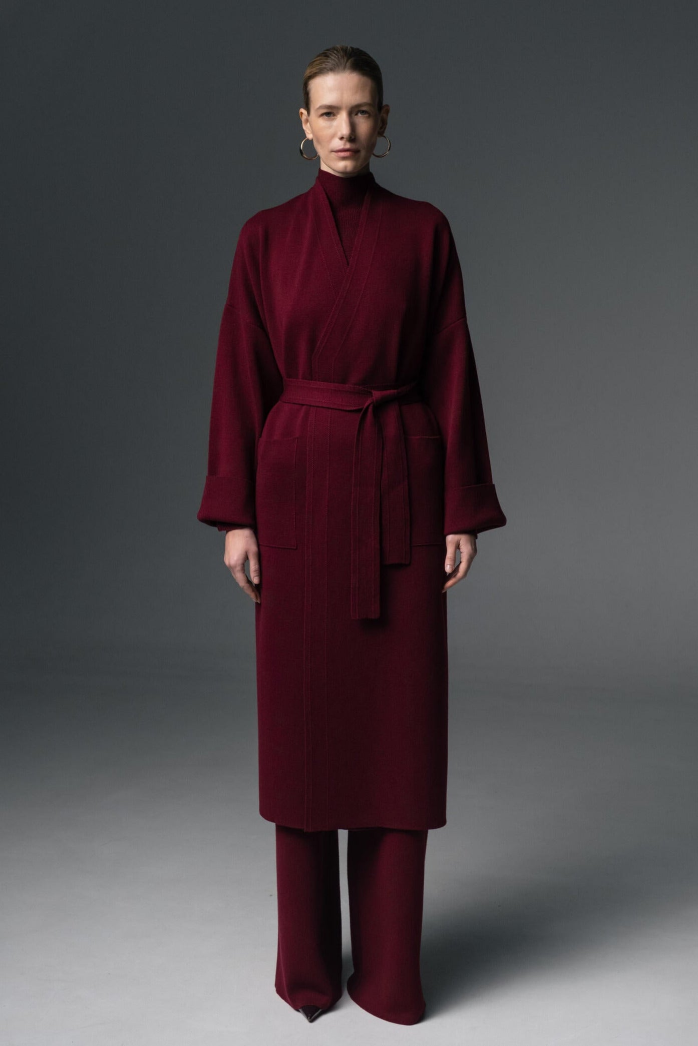 Woman wearing a burgundy coat and pants on a gray background