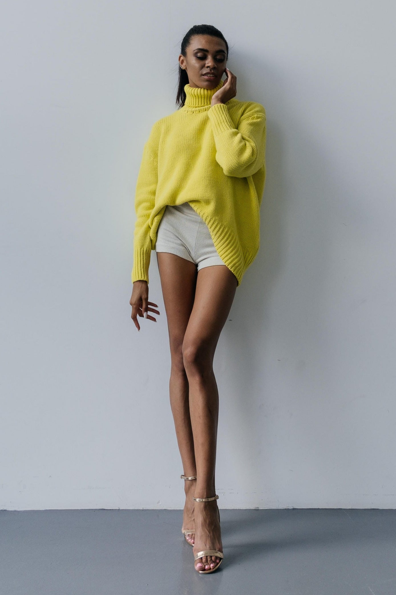 Woman wearing a bright yellow sweater over a white top and shorts against a plain background