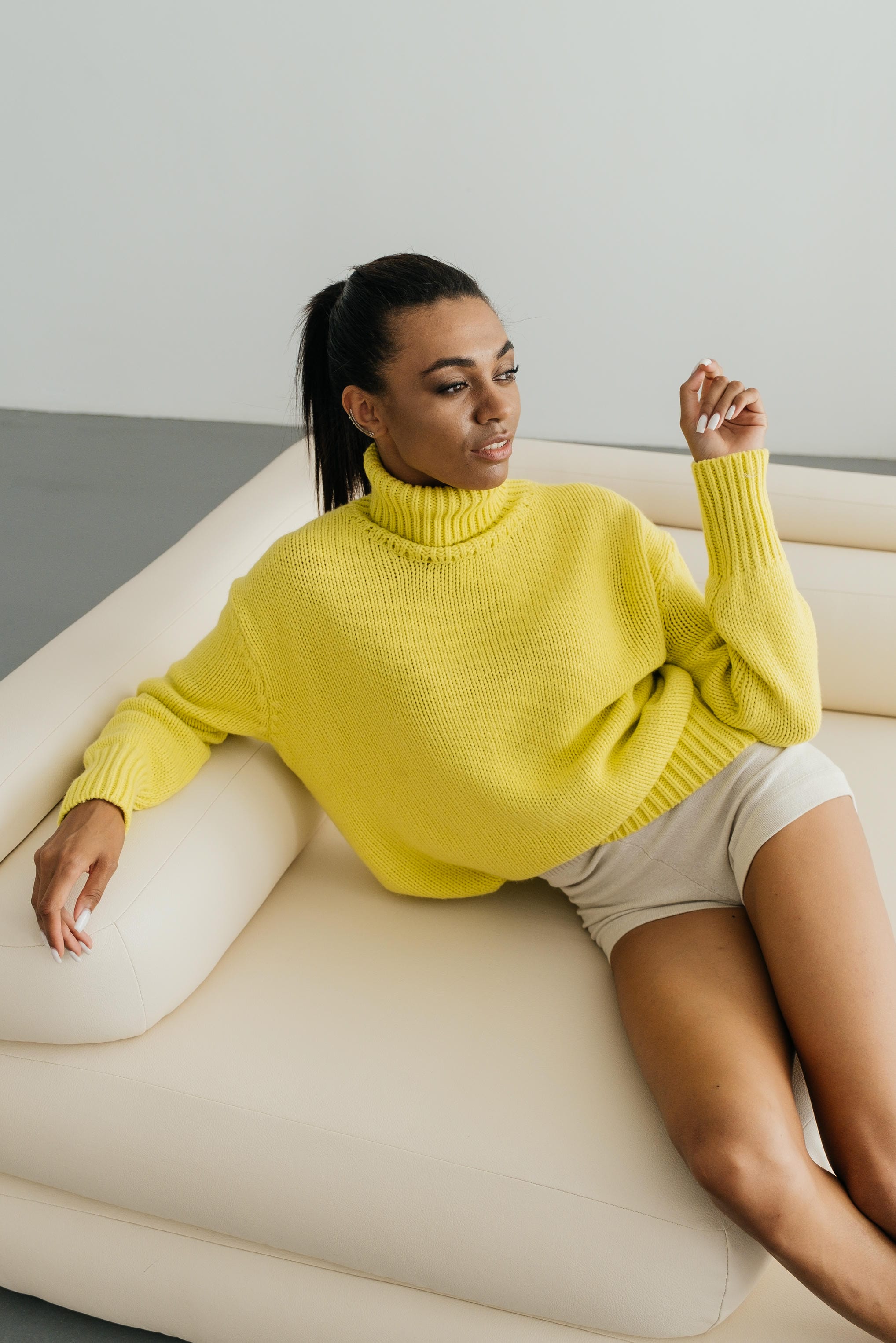 Woman wearing a yellow sweater sitting on a white couch.