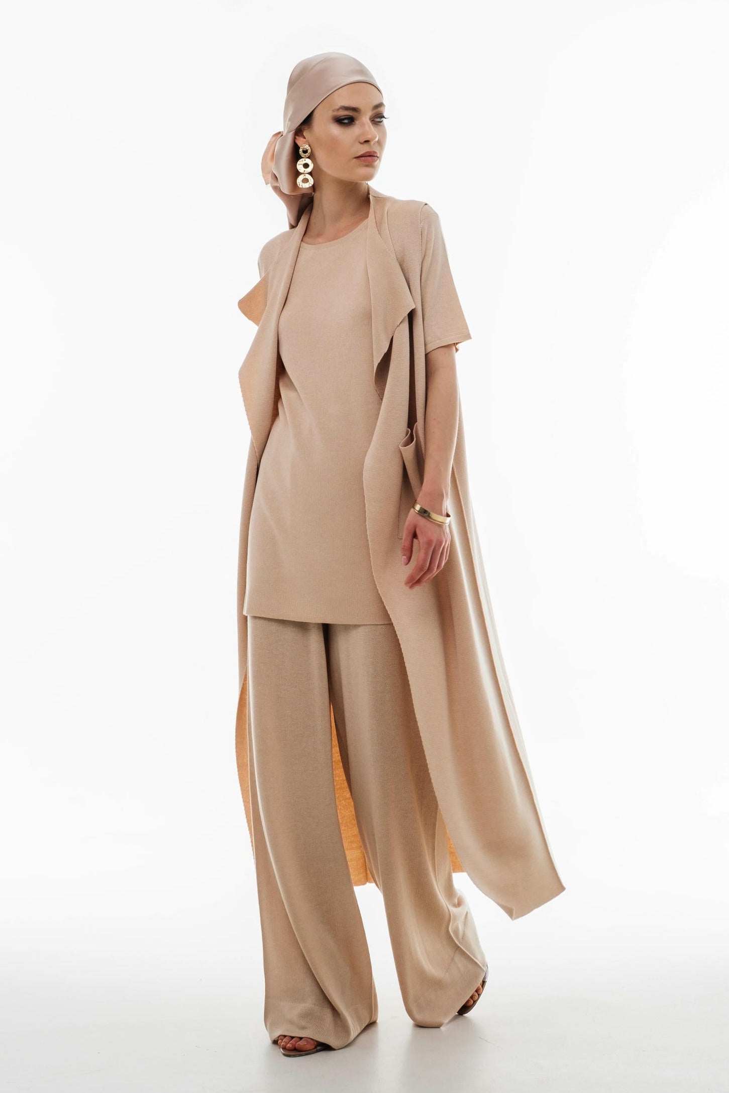 Woman wearing a beige outfit with a long duster on a white background