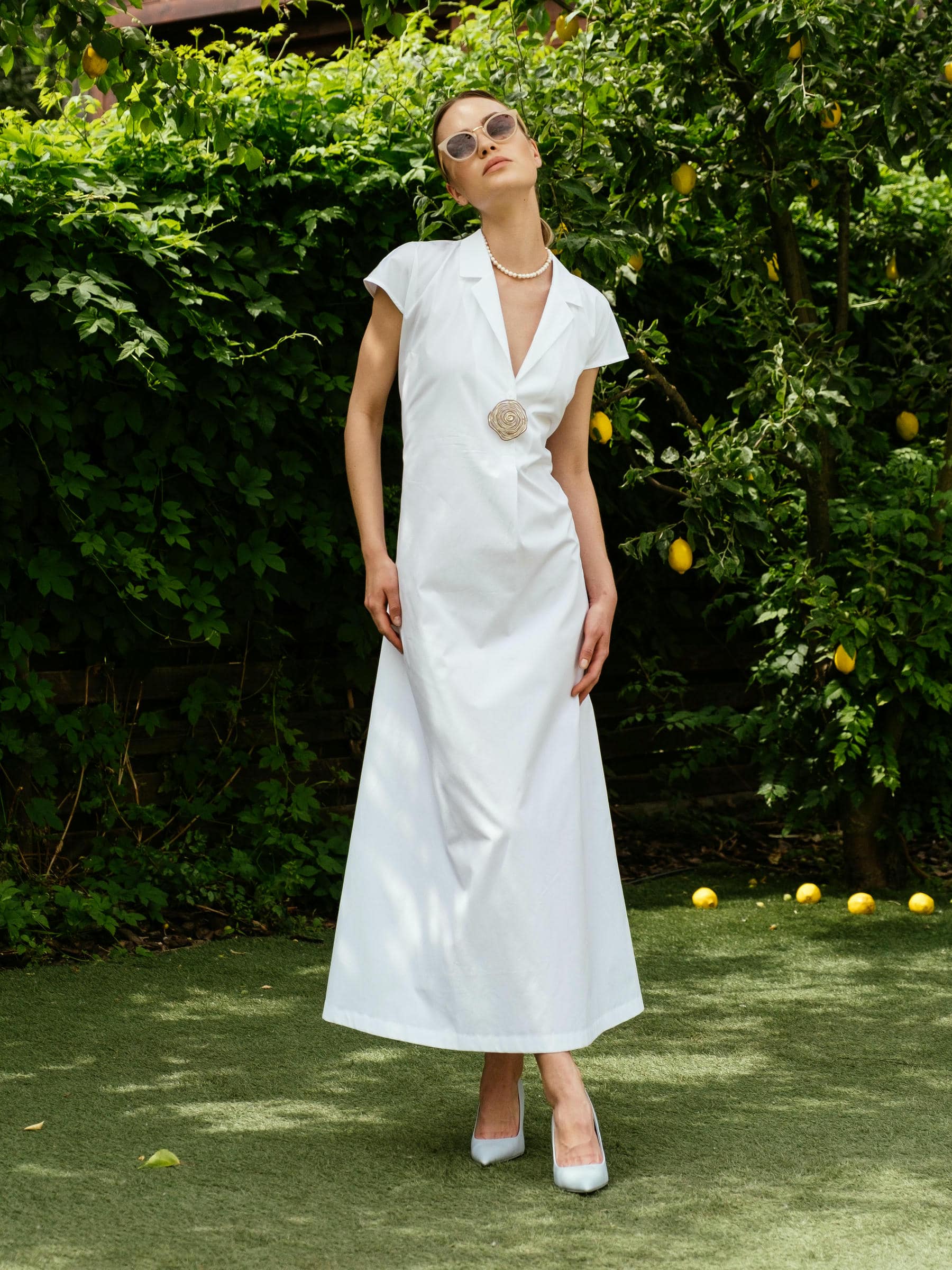 Model wearing white cotton midi dress with lapel front and short sleeves standing in garden – Viamaro