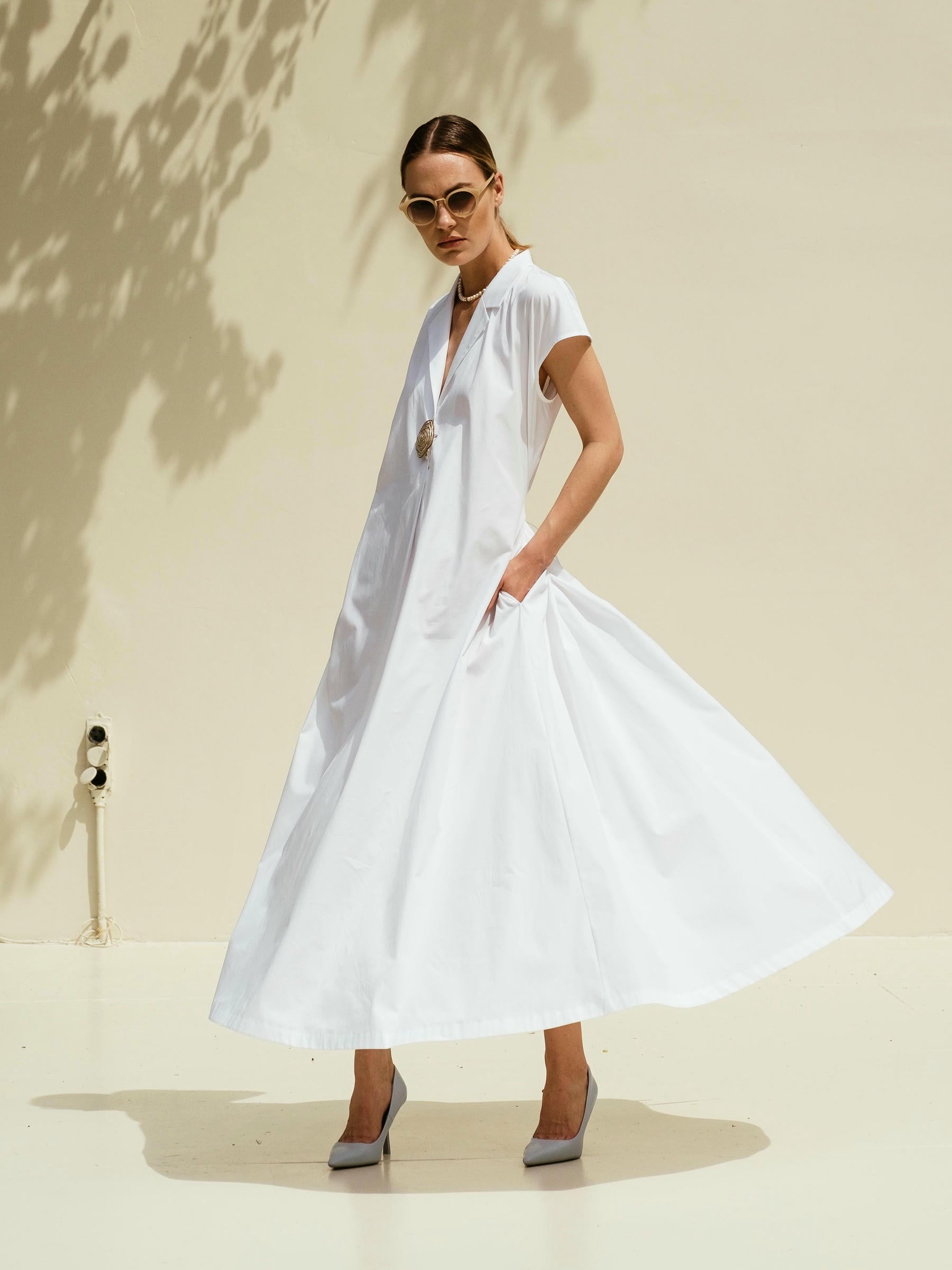 Model wearing white cotton midi dress with lapel front and short sleeves standing in pool setting  – Viamaro
