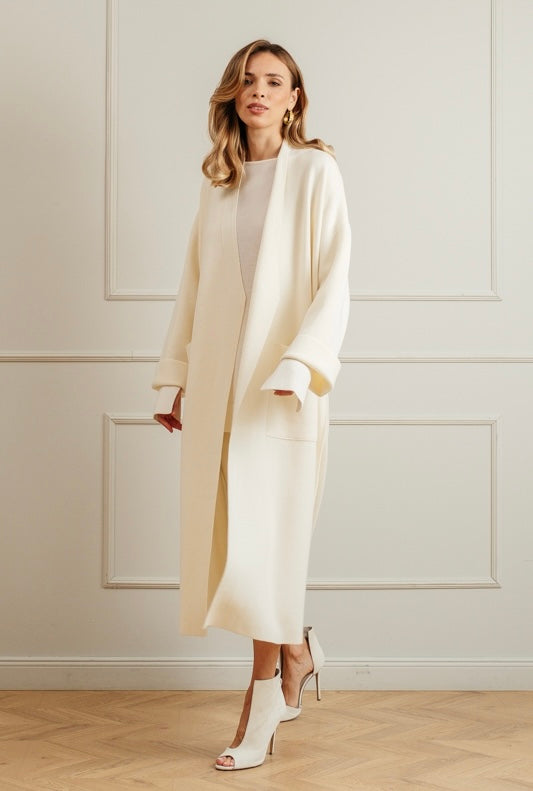 Woman wearing a cream merino wool coat over a minimal knit ensemble, standing in a classic interior.