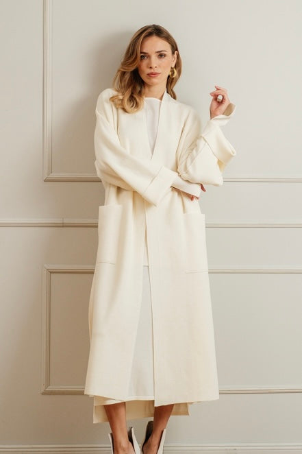 Woman wearing a white merino wool coat over a minimal knit ensemble, standing in a classic interior.