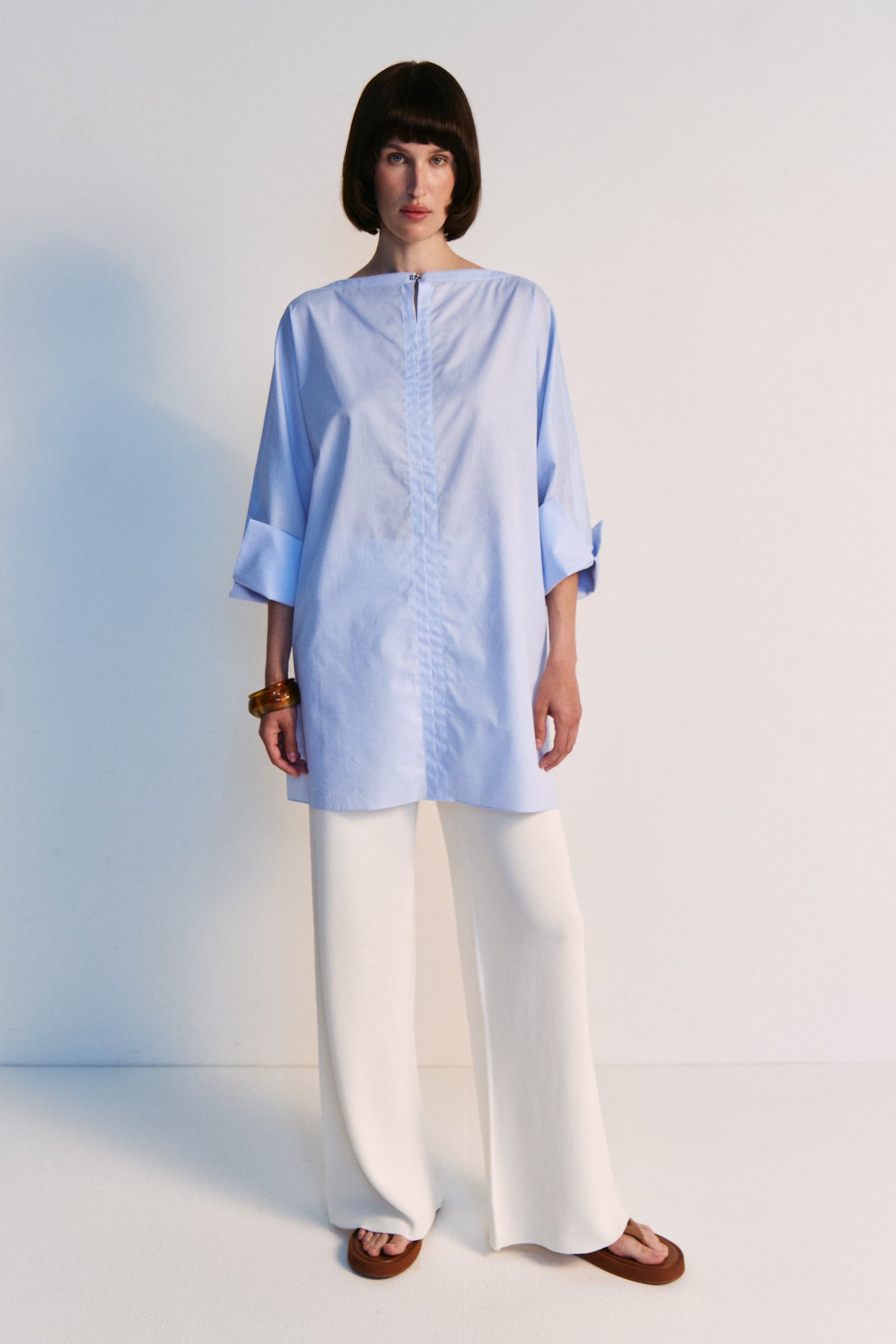 Woman wearing a light blue top and white pants on a plain background