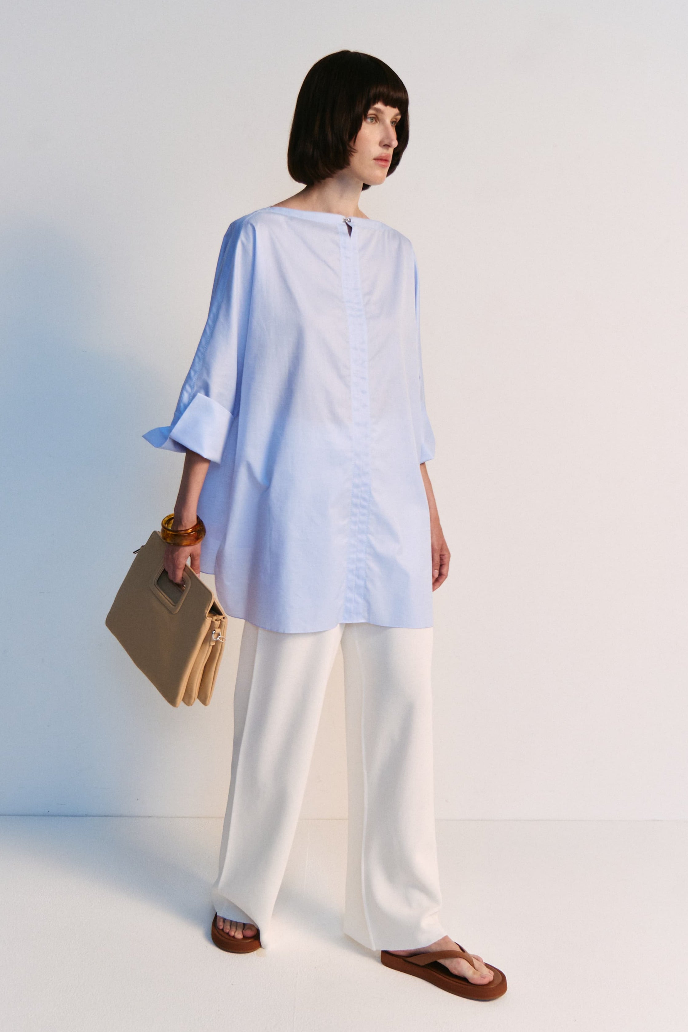 Woman wearing a light blue top and white pants against a white background