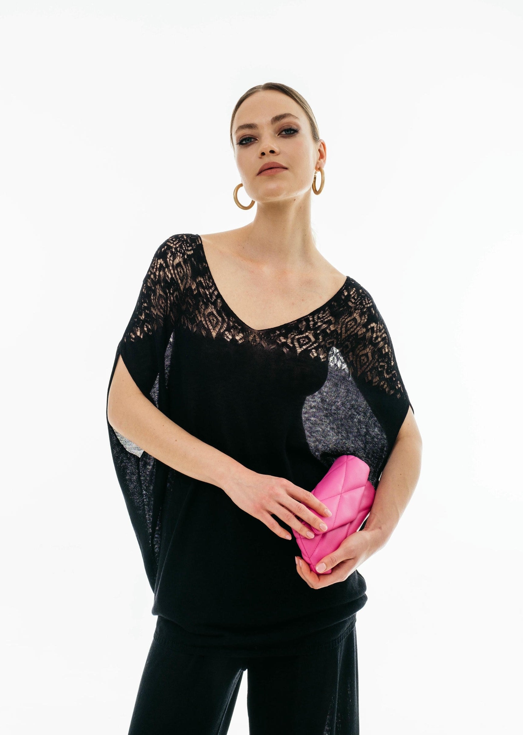 Woman holding a pink clutch wearing a black outfit with lace details on a white background