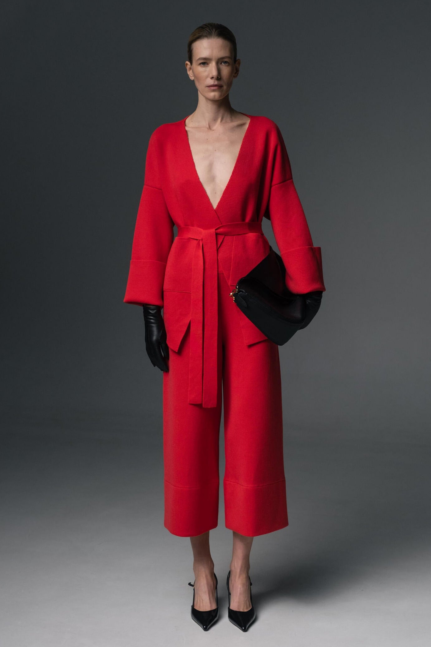 Woman wearing a red outfit with a black clutch against a gray background