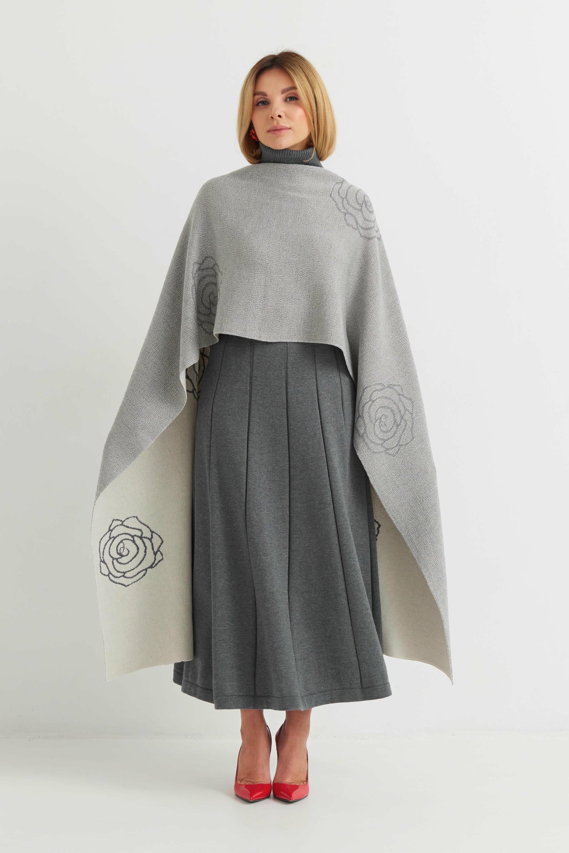 Woman wearing a gray poncho with floral patterns over a gray dress on a white background