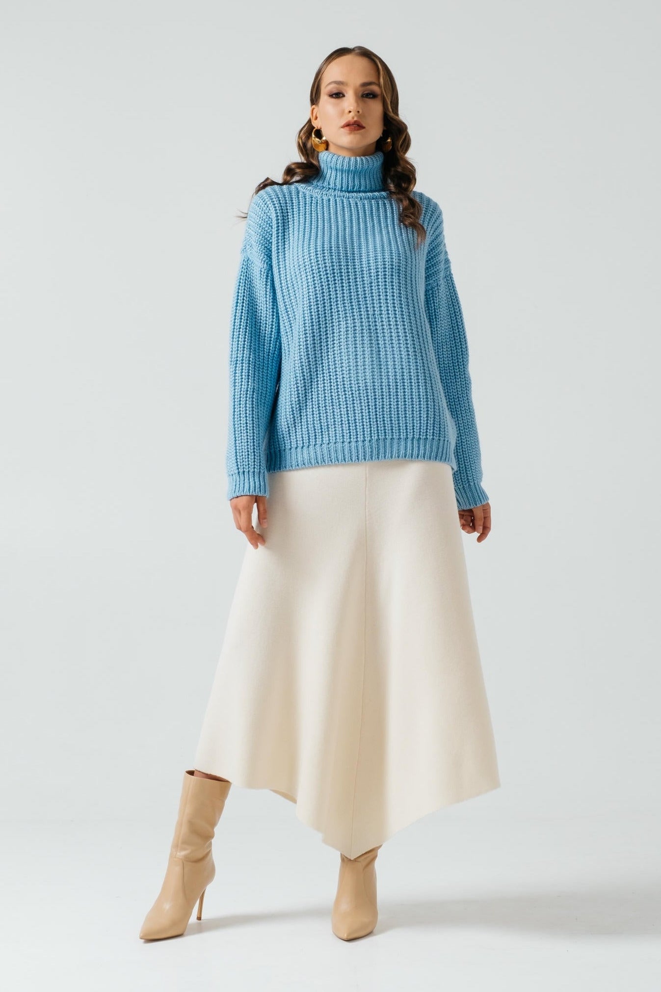 Woman wearing a blue sweater and white skirt on a light gray background