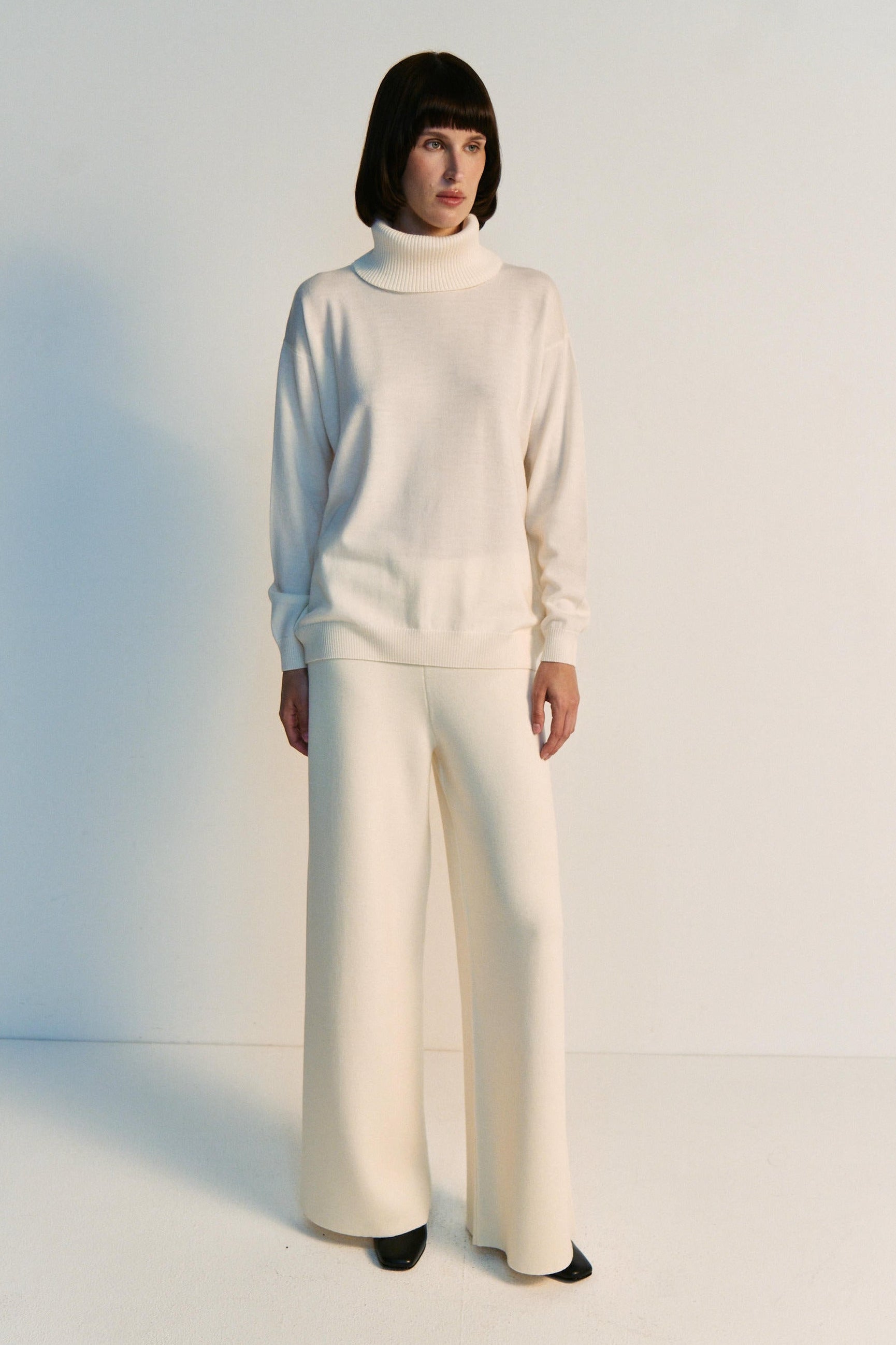 Person wearing a white outfit with wide-leg pants on a plain background
